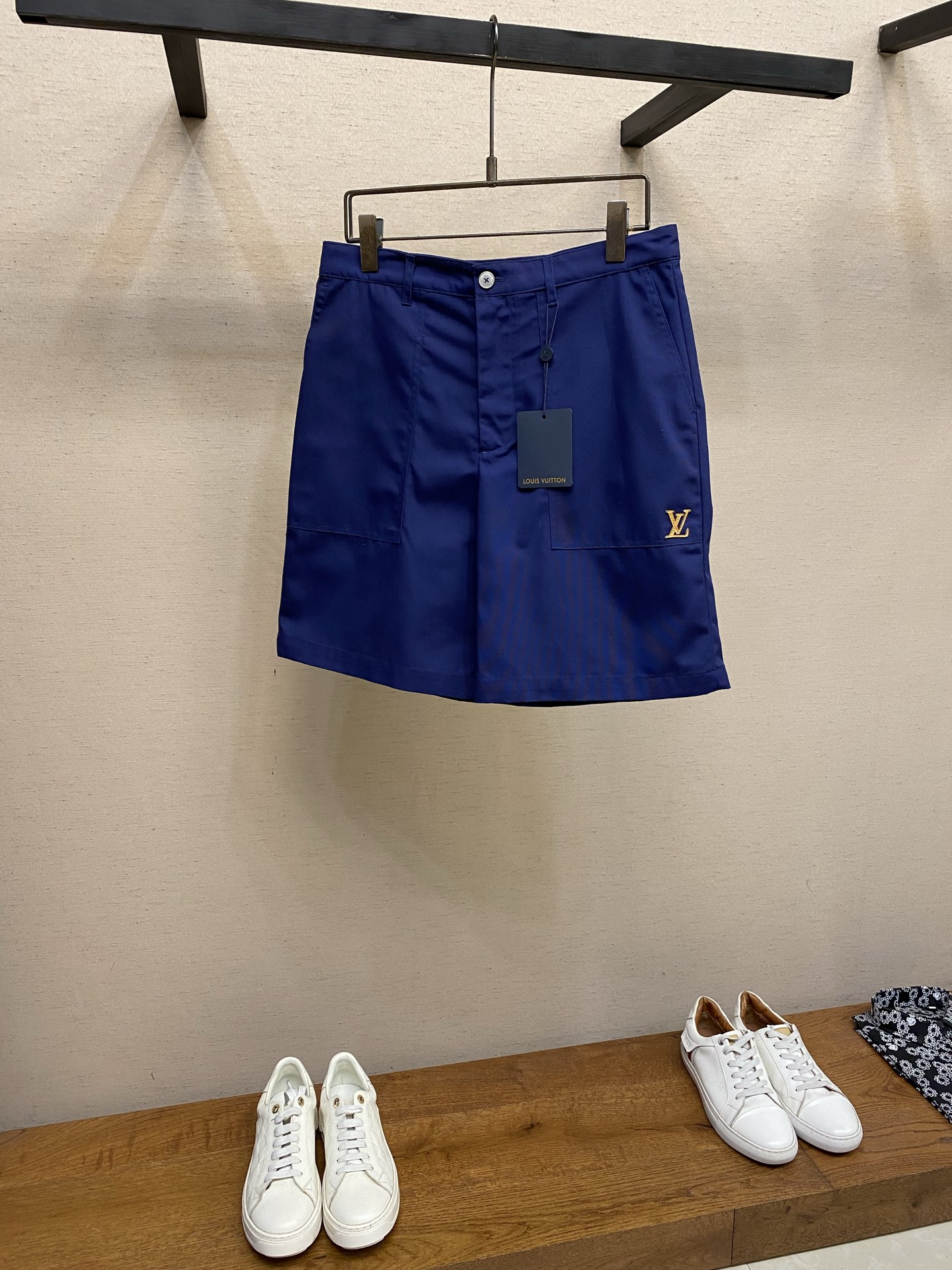 NO:828808,V, referred to as leather work shorts. Original purchase; blended fabric material, VVN leather style logo patch on the left front pocket, Italian style pockets with workwear style topstitching, pearlescent button closure, welted back pockets, full set of accessories # blended cotton woven fabric  The shorts are made of blended materials, with cotton providing stiff silhouette support, sheep wool and mulberry silk contributing to the soft touch and low-key luster respectively, and viscose fiber further improving the smoothness of drape. This ratio not only retains the muscular feel required for workwear, but also uses natural animal fibers to escape the simple texture of pure cotton.  Cotton provides excellent moisture absorption and breathability and wearing comfort, making the fabric soft and skin-friendly; sheep wool gives the fabric good elasticity and shape retention, while increasing warmth and natural drape; viscose fiber improves the drape and gloss of the fabric, making the texture smoother; mulberry silk brings a delicate luster and luxurious touch, enhancing the overall style. # The left front pocket is decorated with a leather-style logo patch  The leather is Louis Vuitton's signature natural vegetable-tanned leather. It has not been dyed and shows the original tone and texture of the original leather. When making the patch, the logo shape is accurately cut out by laser cutting, and the edges are polished to prevent burrs. Patch and pocket  The cloth surface is fixed using precision sewing technology, with fine stitches along the edge of the patch, with even stitch spacing and regular stitches. This process is characterized by high firmness and strong decorative properties. At the same time, the vegetable tanned leather will naturally change color over time, forming a unique skin-nurturing effect.  # Italian-style pockets with workwear-style topstitching. The pockets have a three-dimensional patch pocket structure. The bag body is wide and deep. The bottom is pleated or widened to increase storage capacity. The bag cover is opened and closed with light buttons, and the buttons have a smooth surface, forming a subtle contrast with the roughness of the workwear style.  The Italian-style pocket fits the natural insertion angle of the hand, and the edge of the pocket is reinforced with workwear-style topstitching. Double-needle thick stitching is used, and the stitches are exposed, which not only enhances the firmness of the stress-bearing parts, but also strengthens the visual language of workwear aesthetics. The welted back pocket is located on the hip, and the pocket is edged with narrow welting. The structure is simple, forming a traditional and simplified contrast with the front pocket. Sizes XS-L, Louis Vuitton, shorts,19860909V,简称皮革工装短裤 原购买；混纺面料材质、左侧前袋饰有 VVN 皮革风格标识贴饰、意式口袋配以工装风格明线、珠光纽扣开合、嵌线后袋、全套辅料配备 # 混纺棉质梭织面料 短裤采用混纺材质为基地,棉负责挺括的廓形支撑,绵羊毛和桑蚕丝则分别贡献了软糯触感与低调光泽,粘胶纤维进一步提升垂坠顺滑度.这一配比既保留了工装所需的筋骨感,又用天然动物纤维跳脱出纯棉的朴素质感. 棉提供优异的吸湿透气性与穿着舒适度,使面料亲肤柔软；绵羊毛赋予面料良好的弹性与保形性,同时增加保暖性与自然垂坠感；粘胶纤维提升面料的悬垂性与光泽度,使质感更加顺滑；桑蚕丝则带来细腻的光泽与奢华触感,提升整体格调. # 左侧前袋饰有皮革风格标识贴饰 皮革是路易威登标志性的天然植鞣皮革,未经染色处理,呈现原皮的本真色调与纹理.贴饰制作时,先以激光切割精确裁出标识形状,边缘经打磨抛光处理,防止毛边.贴饰与口袋布面的固定采用精密车缝工艺,沿贴饰边缘以细密针脚缝制,针距均匀、线迹规整.该工艺的特点是牢固度高、装饰性强,同时植鞣革会随使用时间自然变色,形成独特的养皮效果. # 意式口袋配以工装风格明线 口袋呈立体贴袋结构,袋身宽大、深度充足,底部通过打褶或加宽设计增加储物容量.袋盖采用光纽扣开合,纽扣表面光滑,与工装风格的粗犷形成微妙反差. 意式口袋贴合手部自然插入角度,袋口边缘以工装风格明线加固,采用双针粗缝线,线迹外露,既增强受力部位的牢固度,又强化了工装美学的视觉语言.嵌线后袋位于臀部,袋口以窄幅嵌线收边,结构简洁,与正面口袋形成繁简对比. 尺码XS-L,,louis vuitton,shorts,,Men's clothing