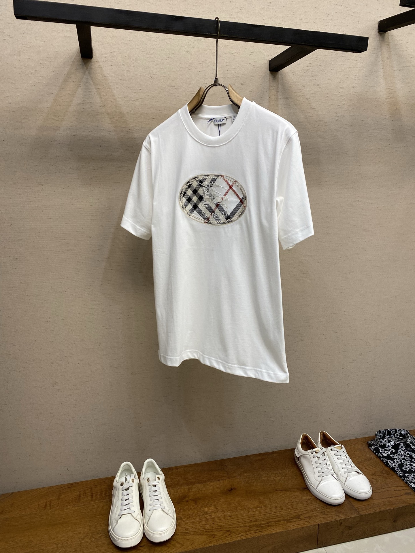 NO:835714,BBR plaid bottom knight round neck short sleeves. Available in black and white. Original purchase; made of medium-thick plain woven cotton fabric, embellished with the same color plaid, knight seal embroidery technology, round-neck casual version, complete set of accessories #Made of medium-thick plain woven cotton fabric It uses 5-count special-spun compact cotton, 230g/㎡, with 32-count 1×1 rib, 340g/㎡. 15-count is a medium-low yarn count. The yarn is thicker and combined with the special-spun compact spinning process, which significantly reduces the yarn hairiness and makes the cloth surface more beautiful. It has a delicate and slightly matte matte texture. The fabric is of medium to high weight, which gives the fabric an excellent bone texture; the neckline uses 32 counts of 1×1 ribs, which makes the neck fibers extremely tight and relies on the physical resilience of the high-density ribs to clamp the neck. # Embellished with the same color plaid knight embroidery process. The plaid knight seal embroidery on the front chest uses a combination of multi-color chain embroidery and twill stitch embroidery. Twill stitch embroidery uses twill-oriented stitches to fill the area within the chain stitch frame. Twill stitch embroidery covers a large area of ​​color through closely arranged parallel stitches, and the twill effect stitches are arranged at specific angles. The diagonal stitches will produce a delicate glossy flow, simulating the visual effect of the twill texture of the fabric. Twill stitching has a stronger three-dimensional effect and resistance to pilling, and can effectively avoid the shrinkage and stiffness of the fabric caused by large-area embroidery. Chain embroidery uses embroidery thread to follow the outline of the plaid and knight's seal and the border of the color block. This stitching method is characterized by a continuous 'V' chain shape on the front and a straight line on the back. It can outline rough and decorative line edges, with a vivid feeling similar to hand-painted graffiti. # Round neck casual version The embroidery pattern is located on the front chest. Since embroidery will reduce the lateral extensibility of the fabric, the designer deliberately retained the loose round neck opening. This design avoids the discomfort caused by the tight neckline and the inability to stretch the front chest, ensuring smooth wearing and taking off of the head. The weight of the fabric has a certain sense of drape, and the decorative center of gravity of the embroidered pattern is on the chest, and the hem usually retains a straight box structure. This design does not cause distortion and wrinkles in the embroidery pattern due to the waist tightening, but also uses the weight of the fabric itself to naturally fall, visually stabilizing the viewer's attention on the craftsmanship highlights of the front chest. The double-needle reinforced stitching on the hem also maintains the overall crisp texture and avoids curling. Size XS-L,, T-shirt,19860909BBR 格纹底骑士圆领短袖 发售色系黑色、白色 原购买；中厚平织棉面料打造、点缀同色系格纹、骑士印章刺绣工艺、圆领休闲版型、全套辅料配备 # 中厚平织棉面料打造 采用5支特纺紧密棉,230g/㎡,搭配32支1×1罗纹,340g/㎡.15支属于中低纱支,纱线较粗配合特纺紧密纺工艺,显著减少了纱线毛羽,使布面呈现出细腻且微雾面的哑光质感.面料属于中高克重,赋予了面料极佳的骨感；领口采用32支1×1罗纹,使领口纤维极度紧实,依靠高密度罗纹的物理回弹力来夹紧颈部. # 点缀同色系格纹骑士刺绣工艺 前胸的格纹骑士印章刺绣采用了多色锁链绣搭配斜纹挨针刺绣的组合工艺. 斜纹挨针刺绣在锁链绣框定的区域内,采用斜纹走向的挨针满幅进行填充.挨针刺绣通过紧密排列的平行针迹覆盖大面积色块,斜纹效果对版针迹按照特定角度排列.斜向针迹会产生细腻的光泽流动感,模拟出织物的斜纹肌理视觉效果.斜纹挨针的立体感和抗起毛性更强,且能有效避免大面积刺绣导致的面料收缩板硬问题. 锁链绣用绣线沿着格纹和骑士印章的轮廓及色块边界进行锁链绣.这种针法的特点是正面呈现连续的“V”字形链条状,背面则是直线.它能够勾勒出粗犷且富有装饰性的线条边缘,具有类似手绘涂鸦的生动感. # 圆领休闲版型 刺绣图案位于前胸位置.由于刺绣会降低面料的横向延展性,设计师特意保留了宽松的圆领开口.这种设计避免了因领口过紧、前胸又无法拉伸而导致的穿着不适感,确保了头部穿脱时的顺畅.面料克重具有一定的垂坠感,配合刺绣图案的装饰重心在前胸,下摆处通常保留了直线的箱型结构. 这种设计既不会因收腰而让刺绣图案产生扭曲褶皱,又能利用面料自身的重量自然下落,在视觉上将观者注意力稳定在前胸的工艺亮点上.下摆的双针加固缝线也维持了整体的挺括质感,避免了卷边. 尺码XS-L,,T-shirt,,Men's clothing