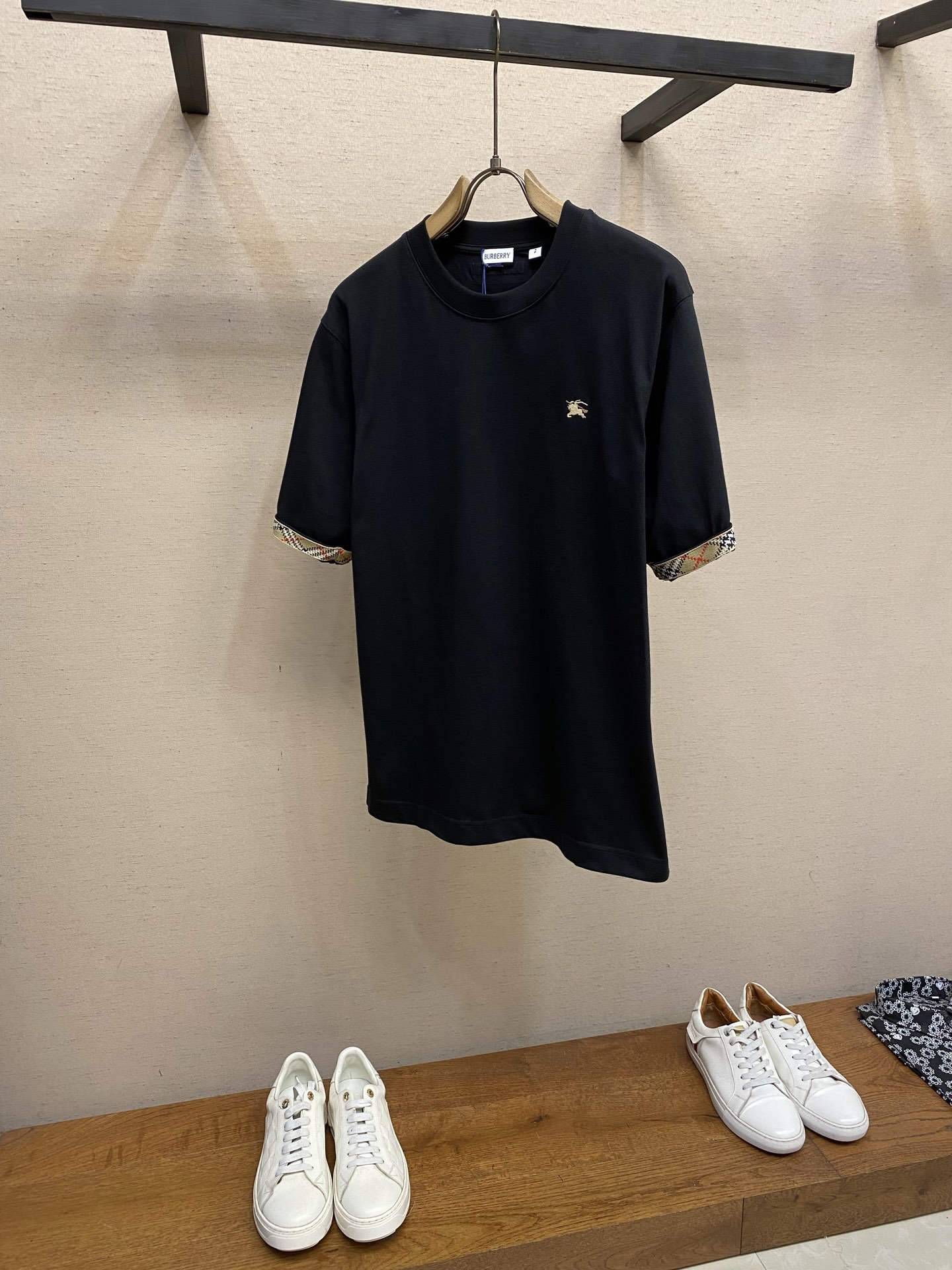 NO:837210,P BBR, plaid round neck short sleeves on sleeves. Available in black and white. Original purchase; Lightweight plain woven compact cotton fabric, embellished with equestrian knight logo embroidery, cuff edges integrated with plaid ribbons, interpretation of iconic sand beige, casual fit, complete set of accessories # Lightweight plain woven compact cotton fabric  Use 15-count special-spun compact cotton, 230g/㎡; match 32-count 1×1 rib, 340g/㎡. The fabric is a heavy-weight fabric with thick needles, strong texture, and crisp texture. Because the 15-count yarn is thicker, the shaping process is particularly important, and it can  It eliminates the internal stress generated during the weaving process of thick yarns and prevents pattern misalignment due to fabric shrinkage during subsequent multi-layer printing. The collar is a high-density tight rib made of cotton, which achieves elasticity through high-density weaving, making the touch more pure and natural.  # Style details of the cuff plaid ribbon The plaid ribbon integrated into the edge of the cuff is the finishing detail of the pattern, and the ribbon completely surrounds the circumference of the cuff. In the pattern design, the sleeve length needs to be compensated and adjusted according to the width of the ribbon. The splicing position of the ribbon is at the edge of the cuff, forming a horizontal dividing line with the sleeve body. This design acts as a horizontal truncation visually, making the sleeve shape more neat, while the sandy beige plaid forms a soft contrast with the main surface tone. #  The layout of the equestrian knight logo. The equestrian knight logo is embroidered using needle embroidery or chain embroidery technology. Before embroidery, a water-soluble lining paper is attached to the back of the base fabric to prevent high-density embroidery from causing wrinkles in the fabric. After the embroidery is completed, the lining paper is removed by washing, leaving a smooth and delicate logo outline.  The equestrian knight logo embroidery is located on the left chest of the chest, forming a classic asymmetrical visual center of gravity with the casual fit. This embroidered logo uses a small size and high-precision processing method, forming a compositional relationship between points and lines with the linear decoration of the cuffs. The logo on the chest is the visual focus, and the plaid ribbon on the cuffs is an extended decorative rhythm. In the pattern design, it is necessary to ensure that the embroidery position is located in the flat area of the chest muscle to avoid embroidery deformation due to human body curves. # Standard casual fit  It adopts a casual version design, which is between the standard version and the loose version. The core feature is that the shoulder line slightly exceeds the acromion point, showing a slight shoulder drop effect; the bust looseness is about 12-16cm compared to the net size, and the body is straight cut; the sleeve shape is wider than standard short sleeves, and the sleeve length is slightly longer. Matched with 230g thick needle weight fabric  When matched, the stiffness of the fabric supports the structure of the casual version - it is neither too loose like the loose version, nor as rigid as the standard version. The advantage of the casual version is that it is 'relaxed and moderate', complementing the classic British temperament of the equestrian knight logo, and is suitable for switching between daily leisure and sports scenes.  Size XS-L,,T-shirt,19860909P BBR,袖边格纹圆领短袖 发售色系黑色、白色 原购买；轻盈平织紧密棉面料、点缀马术骑士徽标刺绣、袖口边缘融入格纹饰带、以标志性沙米色演绎、休闲版型、全套辅料配备 # 轻盈平织紧密棉面料 用15支特纺紧密棉,230g/㎡；搭配32支1×1罗纹,340g/㎡.面料属于粗针重克重面料,肌理感强、质地挺括.由于15支纱线较粗,定形工序尤为重要,它能消除粗支纱线织造过程中产生的内应力,防止后续多层印花时因面料收缩导致图案错位.衣领属于全棉高密度紧实罗纹,全棉罗纹通过高密度织造实现弹性,触感更加纯粹自然. # 袖口格纹饰带的版型细节 袖口边缘融入的格纹饰带是版型的点睛细节,饰带沿袖口圆周完整环绕.在版型设计上,袖长需根据饰带宽度进行补偿调整.饰带的拼接位置位于袖口最边缘,与袖身形成水平分割线.这一设计在视觉上起到横向截断作用,使袖型更显利落,同时沙米色格纹与主面色调形成柔和对比. # 术骑士徽标的版位布局 马术骑士徽标刺绣采用挨针刺绣或锁链刺绣工艺.刺绣前在底布背面贴合可水溶衬纸,防止高密度刺绣导致面料起皱.刺绣完成后通过水洗去除衬纸,留下平整精致的徽标轮廓. 马术骑士徽标刺绣位于胸前左胸位置,与休闲版型形成经典的非对称视觉重心.本款刺绣徽标采用小尺寸、高精度的处理方式,与袖口的线性装饰形成点与线的构图关系.胸前的徽标是视觉焦点,袖口的格纹饰带是延伸的装饰节奏.版型设计中需确保刺绣位置位于胸肌平坦区域,避免因人体曲线导致刺绣变形. # 标准休闲版型 采用休闲版型设计,介于标准版与宽松版之间.核心特点为肩线略微超过肩峰点,呈现轻微落肩效果；胸围松量比净尺寸大约12-16cm,衣身呈直筒剪裁；袖型宽于标准短袖,袖长略长.与230g粗针重克重面料搭配时,面料的挺括性支撑了休闲版型的结构感——既不会像宽松版那样过度松垮,也不会像标准版那样拘谨.休闲版型的优势在于“松弛有度”,与马术骑士徽标的经典英伦气质相得益彰,适合日常休闲与运动场景的切换. 尺码XS-L,,T-shirt,,Men's clothing
