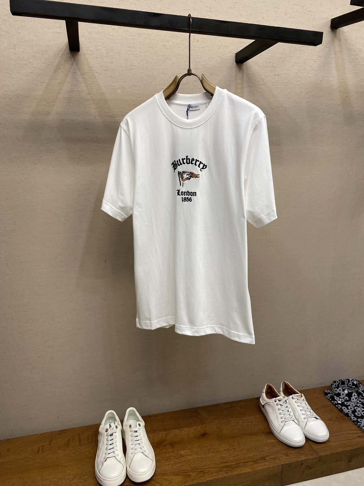 NO:841690,P BBR Flag Pattern Round Neck Short Sleeve. Available in black, white, haze blue. Original purchase; Made of medium-thick plain-woven cotton fabric, embellished with same-color plaids, decorated with new season artistic pattern embroidery, vividly depicting the brand logo, round-neck casual fit, complete set of accessories #Made of medium-thick plain-woven cotton fabric It uses 15-count special-spun compact cotton, 230g/㎡, with 32-count 1×1 rib, 340g/㎡. 15-count is a medium-low yarn count. The yarn is thicker and combined with the special-spun compact spinning process, which significantly reduces the yarn hairiness and makes the cloth surface more beautiful. It has a delicate and slightly matte matte texture. The fabric is of medium to high weight, which gives the fabric an excellent bone texture; the neckline uses 32 counts of 1×1 ribs, which makes the neck fibers extremely tight and relies on the physical resilience of the high-density ribs to clamp the neck. # Decorative New Season Art Pattern Embroidery The checkered flag area uses chain embroidery as the base. Chain embroidery is characterized by a continuous 'V'-shaped chain on the front and a straight line on the back. It covers a large area of ​​color and forms a rough and decorative texture, which has a vivid feeling similar to hand-painted graffiti. After chain embroidery is used as the base, the flag area shows an obvious longitudinal texture, forming a visual rhythm change with the dividing lines of the checkered pattern. The needle-stitch embroidery knight logo uses needle-stitch embroidery for fine depiction. The needle-stitch embroidery covers a relatively small area through closely arranged parallel stitches, which can achieve a smooth, dense and glossy embroidery surface. This stitch method is suitable for expressing delicate and three-dimensional pattern edges. The color of the embroidery thread of the equestrian knight logo forms a clear contrast with the plaid flag, making the logo stand out from the background. The three-dimensional flat stitch embroidery letter part adopts the three-dimensional flat stitch embroidery process. The core feature is that the stitches are tight and flat, completely covering the underlying fabric, and forming a smooth satin-like effect through parallel arranged embroidery threads. This process has no thickness stacking and relies on high-density stitch length and precise thread direction to give the embroidered surface a delicate luster and excellent wear resistance. # Round neck casual version The high weight of the fabric brings a sense of drape, and the center of decoration of the embroidery pattern is on the chest. The hem retains a straight box structure; the embroidery pattern will not be distorted and wrinkled due to the waist tightening, and the weight of the fabric itself can be used to naturally fall, visually stabilizing the focus on the craftsmanship highlights of the chest. The hem uses double-needle reinforced stitching to maintain the overall crisp texture and avoid curling. Sizes XS-L, T-shirt,19860909P BBR 旗帜图案圆领短袖 发售色系黑色、白色、雾霾蓝 原购买；中厚平织棉面料打造、点缀同色系格纹、装饰新季艺术图案刺绣、生动描绘品牌徽标、圆领休闲版型、全套辅料配备 # 中厚平织棉面料打造 采用15支特纺紧密棉,230g/㎡,搭配32支1×1罗纹,340g/㎡.15支属于中低纱支,纱线较粗配合特纺紧密纺工艺,显著减少了纱线毛羽,使布面呈现出细腻且微雾面的哑光质感.面料属于中高克重,赋予了面料极佳的骨感；领口采用32支1×1罗纹,使领口纤维极度紧实,依靠高密度罗纹的物理回弹力来夹紧颈部. # 装饰新季艺术图案刺绣 格纹旗帜格纹旗帜区域采用了锁链绣作为基础打底.锁链绣的特点是正面呈现连续的“V”字形链条状,背面则是直线.覆盖大面积色块同时形成粗犷且富有装饰性的纹理,具有类似手绘涂鸦的生动感.锁链绣打底后,旗帜区域呈现出明显的纵向肌理感,与格纹的分割线条形成视觉上的节奏变化. 挨针刺绣骑士标识则采用了挨针刺绣进行精细刻画.挨针刺绣通过紧密排列的平行针迹覆盖相对较小的区域,能够实现平滑、密实且具有光泽感的绣面.这种针法适合表现精致、立体的图案边缘.马术骑士徽标的绣线色彩与格纹旗帜形成明显反差,使徽标从背景中跃然而出. 立体平针刺绣字母部分采用立体平针刺绣工艺,核心特点是针迹紧密平整、完全覆盖底层面料,通过平行排列的绣线形成光滑如缎面的效果.该工艺没有厚度堆叠,依靠高密度针距和精准的走线方向,使绣面呈现出细腻的光泽感和极佳的耐磨性. # 圆领休闲版型 面料中高克重带来的垂坠感,配合刺绣图案的装饰重心在前胸,下摆保留了直线的箱型结构；既不会因收腰而让刺绣图案产生扭曲褶皱,又能利用面料自身的重量自然下落,在视觉上将注意力稳定在前胸的工艺亮点上.下摆采用双针加固缝线,维持了整体的挺括质感,避免了卷边. 尺码XS-L,,T-shirt,,Men's clothing