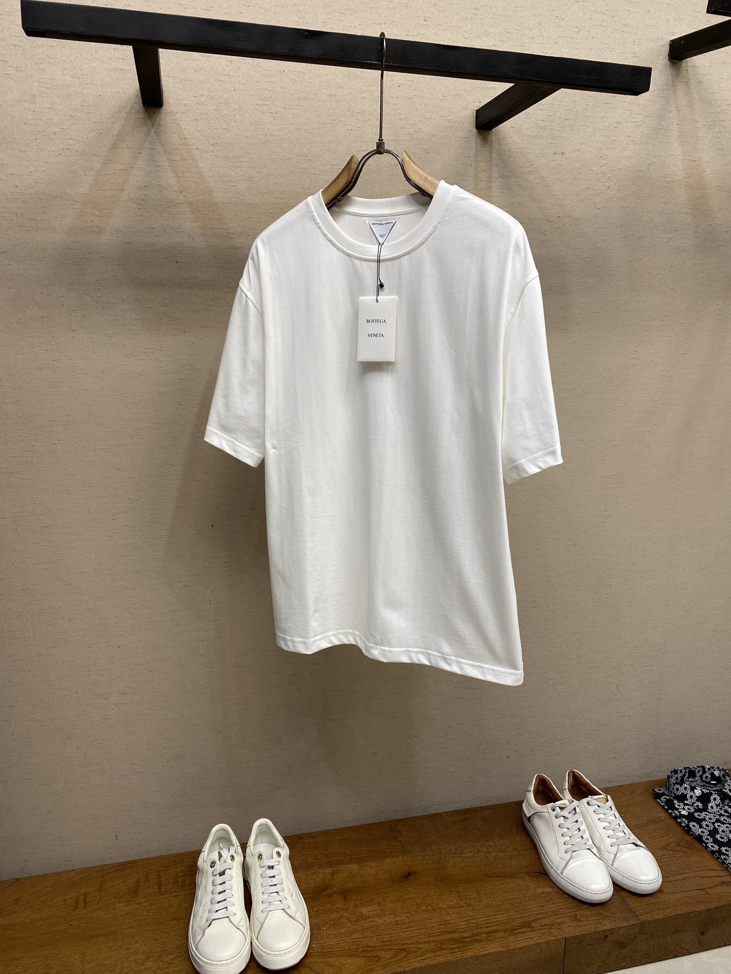 NO:848424,P BV, woven triangle round neck short sleeves. Original purchase; pure cotton plain fabric, sheep wool woven triangle patch, round neck loose version, full set of accessories # pure cotton plain fabric The fabric is made of 15-count special-spun compact cotton, 230g/m; paired with 32-count 1×1 rib, 340g/m. The 15-count special-spun compact cotton is a medium-low yarn count, and the yarn is thicker. The special-spun compact spinning process significantly reduces yarn hairiness, allowing even thick-count yarns to present a delicate and microscopic appearance. The matte cloth texture also greatly improves the anti-pilling level. The medium and high weight gives the fabric an excellent bone texture, and the cloth woven from roving has a more obvious yarn texture and micro-graininess. The 32-count high-density rib locking neckline is stable, high-strength binding, and can firmly lock the neck arc. # Sheep Wool Woven Triangular Patch Wool fiber has natural curl elasticity and matte luster. After being woven into a triangle shape, the patch presents a fluffy and soft touch and rich texture levels that are different from cotton fabrics. The natural tone of wool forms a material contrast with the pure cotton T-shirt. The stiffness and dryness of cotton and the softness and warmth of wool create a visual and tactile collision. Thin cotton threads of the same color are used for high-density sewing and fixation along the edge of the patch, which not only ensures firmness, but also makes the stitching itself a decorative element. # Conventional round neck version This short-sleeved shirt adopts a conventional round neck loose version, with precise tailoring and smooth lines. The shoulder line is processed naturally, which can highlight the wearer's shoulder lines without restricting the freedom of movement, making the clothing comfortable to wear. The neckline is uniquely designed, with strong tightening of high-density ribbing. The sleeve type is wide short-sleeved, with fine cuffs and hem, and a simple structure. Sizes XS-L,,bottega veneta,T-shirt,tees,t-shirt,19860909P BV,编织三角圆领短袖 原购买；纯棉质平纹面料、绵羊毛编织三角贴饰、圆领宽松版型、全套辅料配备 # 纯棉质平纹面料 面料采用15支特纺紧密棉,230g/m；搭配32支1×1罗纹,340g/m.15支特纺紧密棉属于中低纱支,纱线较粗.特纺紧密纺工艺显著减少了纱线毛羽,使粗支纱线也能呈现出细腻且微雾面的布面质感,同时大幅提升抗起毛球等级.中高克重赋予了面料极佳的骨感,粗纱织出的布面具有更明显的纱线肌理和微颗粒感.32支高密度罗纹锁定领口稳定,高强度收束,能牢牢锁定颈部弧线. # 绵羊毛编织三角贴饰章仔 羊毛纤维具有天然的卷曲弹性、哑光光泽.编织成三角形状后,章仔呈现出不同于棉织物的蓬松柔软触感和丰富的纹理层次.羊毛的天然色调与纯棉T恤形成材质对比,棉的挺括干爽与羊毛的柔软温暖,视觉和触觉上都有碰撞感.用同色系的细棉线沿章仔边缘进行高密度缝制固定,既确保牢固度,又让缝线本身成为装饰元素. # 常规圆领版型 这款短袖采用常规圆领宽松版型,剪裁精准、线条流畅.肩线处理自然,既能够凸显穿着者的肩部线条,又不会限制活动自由度,使衣物在穿着时保持舒适.领口设计独特,配合高密度罗纹的强力收束,袖型为宽大短袖,袖口与下摆均采用精细收口,结构简洁. 尺码XS-L,,bottega veneta,T-shirt,tees，t-shirt,,Men's clothing