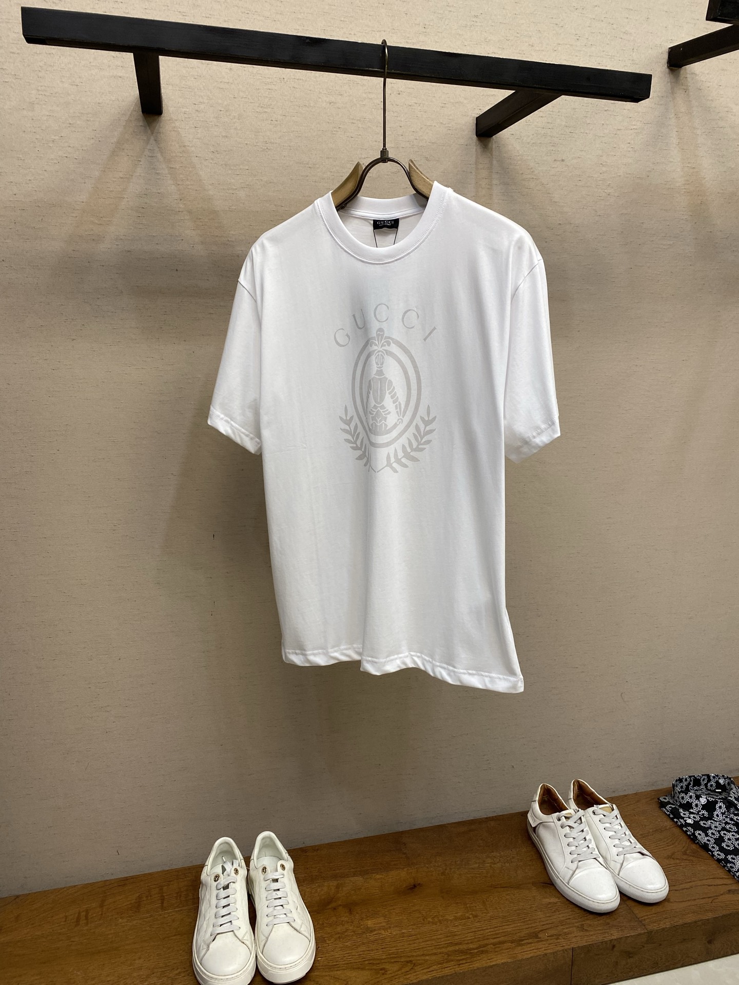 NO:848427,PGucci, armor logo round neck short sleeves, available in black and white, original purchase; pure cotton jersey fabric, Gu armor badge printing, round neck short sleeve version, #matched version developed new black accessories, equipped with # double-sided fine count structure pure cotton fabric  It uses 24 counts of double-sided knitted cotton, 250g/m, with 24 counts of 1×1 rib, 200g/m. The 24-count yarn is a medium-to-high fine count yarn with a thin yarn diameter. The double-sided knitted structure has the fluffy and soft hand unique to double-sided knitting.  feeling without losing drape support. The cloth surface is more delicate, smooth and compact, with smaller gaps between fibers, and the touch is close to the exquisiteness of high-density poplin. This delicate base gives the T-shirt a silky matte texture and has good anti-pilling properties.  # Black model uses powder paste printing process. The black model uses powder paste printing, which is essentially a water-based glue with strong covering power. It is suitable for printing light-colored patterns on dark fabrics. Powder paste printing can present a saturated, bright and sharp-edged pattern effect on a black base. Its covering layer has a certain thickness and will have a slight gelatinous feel to the hand; it presents a saturated, bright and sharp-edged pattern effect. # White model penetration printing  The white model uses a penetration printing process. Penetration printing is essentially dye printing. Special additives are used to completely penetrate the dye molecules into the cotton fiber and form a covalent bond with the fiber. The thickness and softness of the fabric in the printed area and the blank area are exactly the same, maintaining the original silky touch of 24-count double-sided cotton. The color fastness of penetration printing is extremely high, and there will be no common cracking or shedding of glue after multiple washes. # Conventional round neck design  This short-sleeve design adopts a conventional round neck design, with the shoulder line accurately falling on the acromion point. The body is straight-cut, with similar bust and hem circumferences, fitting but not tight, taking into account free movement and clean lines. The sleeve shape is standard short-sleeved, with fine cuffs and hem, and a simple structure. Sizes XS-L,, gucci, T-shirt, tees, t-shirt,19860909PGucci,盔甲标识圆领短袖 发售色系黑色、白色 原购买；纯棉平纹针织面料、Gu盔甲徽章印花、圆领短袖版型、#对版开发新款黑色辅料配备 # 双面细支结构纯棉面料 采用用了24支双面针织棉,250g/m,搭配24支1×1罗纹,200g/m.24支属于中高细支纱线,纱线直径较细.双面针织结构既有双面针织特有的蓬松柔软手感,又不失垂坠支撑力.布面更加细腻、光滑且紧致,纤维间空隙更小,触感接近高密府绸的精致度.这种细腻的基底使T恤呈现出丝滑的哑光质感,具有良好的抗起毛球性能. # 黑色款粉浆印花工艺处理 黑色款采用粉浆印花本质上是一种遮盖力极强的水性胶浆,适合在深色面料上印制浅色图案.粉浆印花在黑色基底上能呈现饱和、明亮且边缘锐利的图案效果.其覆盖层具有一定的厚度,手感上会有轻微的胶质感；呈现饱和、明亮且边缘锐利的图案效果. # 白色款渗透印花 白色款则采用了渗透印花工艺,渗透印花本质上是染料印花,通过特殊助剂使染料分子完全渗入棉纤维内部,与纤维发生共价键结合.印花区域和空白区域的面料厚度、柔软度完全一致,保持了24支双面棉原始的丝滑触感.渗透印花的色牢度极高,多次水洗后不会出现胶浆常见的龟裂或脱落. # 常规圆领版型设计 这款短袖采用常规圆领版型设计,肩线精准落在肩峰点,衣身呈直筒剪裁,胸围与下摆围度相近,合身而不紧身,兼顾活动自如与利落线条.袖型为标准短袖,袖口与下摆均采用精细收口,结构简洁. 尺码XS-L,,gucci,T-shirt,tees，t-shirt,,Men's clothing