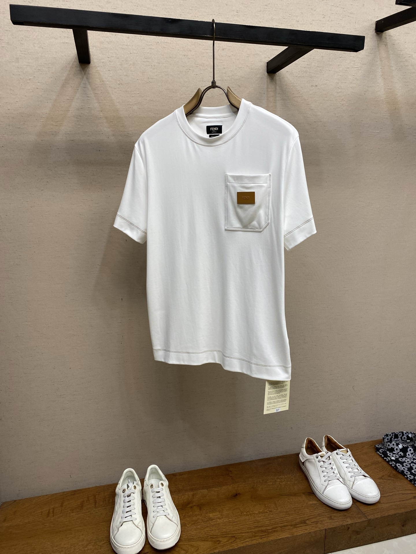 NO:849972,Fendi, short sleeves with leather patches. Fabric selection: High-count combed long-staple cotton fabric is selected and woven. The fiber is fine and compact, and the cloth surface is smooth and smooth. The cotton fiber has excellent breathability, good moisture absorption and perspiration, and the upper body is soft and skin-friendly, not stuffy or sticky. After the fabric is pre-shrunk, sanded and anti-wrinkle shaping process, it drape and stiffness is not easy to collapse, and it is not easy to deform, pill or fade after being washed for a long time, highlighting the solid texture.  Detail 1: It is sewn with vintage brown and yellow contrasting topstitching, and double-needle chain sewing technology is used throughout. The collar, cuffs, hem, breast pockets, and back collar are all evenly routed. The contrasting line and the white background form a natural transitional visual hierarchy. The spacing between stitches is even and regular, and the two lines are parallel and straight and smooth. It not only strengthens the structural shape, strengthens the firmness of the body, and is not easy to collapse and crack, but also uses extremely simple open thread to outline a high-end texture. Detail 2  The chest patch bag is three-dimensionally cut, and the bag mouth is shaped by high temperature. The bag body is flat and compliant, and the bag edges are double-needle overlock seamed, which is strong and wear-resistant. The details of the patch bag are made of custom leather. The leather is flexible and shiny, and the edges are polished and sealed. The letter logo is engraved using high-temperature embossing process, and the font is clear and neat. The edges of the leather label are precision sewn and fixed to the bag body, and the wiring is tight and neat. Detail 3  The back of the collar is sewn with square decorative stitches using special wood pulp fiber sutures. The wood pulp fiber threads are strong in toughness, not easy to break, and have a warm color. The square lines are neatly symmetrical, echoing the contrasting topstitching style throughout the body, and are both decorative and reinforcing. Sizes S-XL,, fendi, T-shirt,19860909Fendi,饰皮革贴片短袖 面料选择 甄选高支精梳长绒棉面料织造,纤维细腻紧实,布面平整顺滑.棉纤维自带优良的透气性,吸湿排汗性俱佳,上身柔软亲肤,不闷不粘.面料经过预缩、磨毛与抗皱定型工艺处理之后,垂坠挺括不易软塌,久洗不易变形、不起球、不褪色,凸显扎实的质感.  细节1 采用复古棕黄撞色明线精工缝制,全程采用双针链式车缝工艺,领口、袖口、下摆、胸袋、后领无一例外均匀走线.撞色线与白底色形成自然过渡的视觉层次,针脚间距均匀规整,双线平行笔直流畅,不仅强化结构定型,加固衣身牢固度,不易崩线开裂,更用极简明线勾勒出高级质感. 细节2 胸贴袋采用立体剪裁,袋口经过高温定型,袋身平整服帖,袋边双针包边锁缝,牢固耐磨；贴袋点缀的细节选用定制皮革,皮料柔韧有光泽,边缘经打磨封边,再采用高温压印工艺刻印字母标识,字体清晰工整.皮标边缘精密车缝固定于袋身,走线密实工整. 细节3 衣领背部采用木浆纤维专用缝线缝制方形装饰线迹,木浆纤维线材韧性强、不易断裂、色泽温润,方形走线工整对称,与全身撞色明线风格呼应,兼具装饰性与加固作用. 尺码S-XL,,fendi,T-shirt,,Men's clothing
