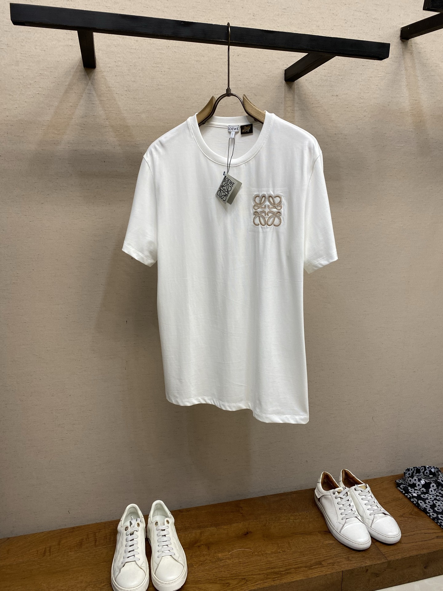 NO:849989,Loewe, lightweight cotton embroidered short-sleeve fabric selection. Select high-count lightweight combed cotton fabric, which has a soft and delicate touch, excellent breathability and perspiration, and the upper body is refreshing and not sweaty. After the fabric is finely preshrunk and smoothed, it is not easy to deform and wrinkle, and remains stiff and stylish for a long time. It is skin-friendly and does not prick the skin, taking into account both comfortable body feel and drape texture. Embroidery process  The iconic two-color Anagram three-dimensional embroidery on the chest is precision woven using a high-end Tajima embroidery machine. First, a precise calculation system is used to accurately locate the embroidery mark points on the body, and the double-layer seam is reinforced as a base, and then light brown + off-white two-color embroidery thread is used.  The three-dimensional hook stitch method is stacked layer by layer, and the pattern is intertwined to outline the pattern logo. Each stitch is evenly and fullly routed, the coil texture is clear and three-dimensional, the edges are neat and lint-free, and the embroidery fits closely with the fabric without being tight or warping, presenting a high-grade relief texture.  Detail 1: The reverse side of the embroidery is covered with four-sided elastic interlining of the same color, so that it sticks to the skin without digging into the flesh, improving the wearing experience. Detail 2:  The round neck is matched with a high-elastic rib collar, and the stitching is dense and neat. It will not loosen and deform after being washed for a long time, and it fits the neck line without pinching the skin. The cuffs are made of double-needle topstitching technology, with fine and even stitches, and the stitching is firm and flat, making it durable and wear-resistant and not easy to fall off. The side seams of the body are made of seamless hemming, and the stitching is straight and smooth without excess thread. The hem is regular and neat, and the overall shape is smooth and smooth.  Size S-XL,,loewe,T-shirt,19860909Loewe,轻盈棉质饰刺绣短袖 面料选择 甄选高支轻盈精梳棉面料,其触感软糯细腻,透气排汗性出众,上身清爽不闷汗.面料经过精细预缩与柔顺处理之后,不易变形起皱,长久保持挺括有型,亲肤不扎肤,兼顾舒适体感与垂坠质感. 绣花工艺 胸前标志性双色Anagram立体刺绣,采用高端田岛绣花机精密织造而成.先通过精密计算系统精准定位衣身绣标点位,双层锁边打底加固,再以浅棕+米白双色绣线,运用立体勾线针法层层堆叠,环环交织勾勒图案回纹标识.每一针走线均匀饱满,线圈肌理清晰立体,边缘工整无毛絮,刺绣与面料紧密贴合,不紧绷、不翘边,呈现高级浮雕质感. 细节1 绣花反面覆以同色四面弹力衬布之后贴肤不扎肉,提升穿着体验. 细节2: 圆领搭配高弹罗纹领,锁边走线密实工整,久洗不易松垮变形,贴合颈部线条不勒肤；袖口采用双针明线车缝工艺,针脚细密均匀,锁边牢固平整,耐穿耐磨不易脱线；衣身侧缝采用无痕包边处理,走线笔直顺滑,无多余线头,下摆规整利落,整体版型平整垂顺. 尺码S-XL,,loewe,T-shirt,,Men's clothing