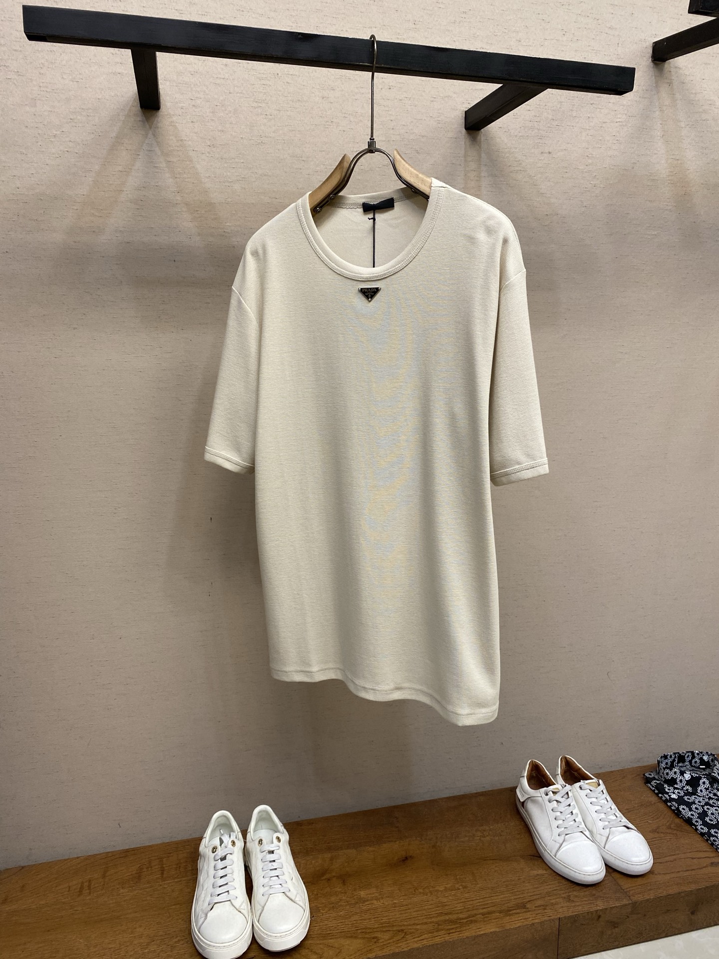 NO:849985,Prada, metal logo waffle T-shirt. Fabric: 24-count double-sided waffle fabric / 250G. Rib: 24-count 1×1 rib / 200G. The design is simple but unique. This T-shirt is made of soft cotton fabric, classic short-sleeved cut, and ribbed knit trim. The enameled metal triangle logo embellishes this piece of clothing.  The 24-count double-sided waffle structure not only ensures the fineness of the fabric, but also avoids looseness caused by being too thin. The double-sided weave allows the waffle texture to present different geometric concavities and convexities on the front and back sides, and the thickness is stable. The fabric is stiff and boney, which prevents the thin waffle from easily deforming; it forms a uniform air layer to enhance breathability while locking in body temperature.  The enamel-coated metal triangular logo process uses a zinc alloy die-cast base to form a sharp triangular outline. A claw nail buckle with a non-slip gasket is welded on the back, which is fixed after penetrating the fabric. The glassy glaze is filled into the metal recessed area and is fired at high temperature to form a smooth, wear-resistant and never-fading glaze layer. Sizes XS-L,, prada, T-shirt, tees, t-shirt,19860909Prada,金属徽标华夫格T恤 面料24支双面华夫格纹面料 / 250G 罗纹24支1×1罗纹 / 200G 设计简约但风格特别,这款T恤采用柔软棉质面料,经典短袖剪裁,配以罗纹针织饰边.涂珐琅金属三角形徽标装饰这件衣服. 24支双面华夫格结构既保证了织物的细腻度,又避免了过薄导致的松垮.双面织法令华夫格纹理在正反面呈现不同几何凹凸感,且厚度稳定.面料挺括有骨感,避免了轻薄华夫格易变形；形成均匀的空气层,增强透气性的同时锁住体感温度. 涂珐琅金属三角形徽标工艺上采用锌合金压铸基底,形成锐利的三角形轮廓,背面焊有带防滑垫片的爪钉扣,穿透面料后固定.将玻璃质釉料填入金属凹陷区域,经高温烧制后形成光滑、耐磨、永不褪色的釉面层. 尺码XS-L,,prada,T-shirt,tees，t-shirt,,Men's clothing