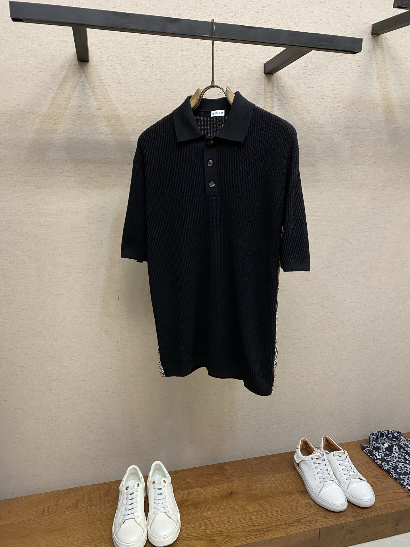 NO:930950,BBR, plaid decorative knitted POLO shirt fabric weaving  The main body is made of high-count lightweight cotton yarn, using vertical pit rib knitting technology. The yarn is plied and shaped, and is woven with a circular knitting machine to create a three-dimensional vertical grain texture. The special weaving method forms an internal air layer in the fabric, which is soft and not heavy to the touch, taking into account both breathability and drape. The texture of the cloth surface is even and regular, and it is not easy to deform and wrinkle. After multiple washings, the pit strips are still clear and three-dimensional, making it comfortable to wear without restraint. Detail 1  The two sides of the body are spliced with retro plaid knitted webbing, using synchronous jacquard knitting technology. The plaid is woven simultaneously with multi-color yarns, with clean color boundaries and no halo jumpers. The webbing and trousers body panels are precisely sewn and spliced, and the lines are straight and firm. The classic plaid elements break the monotony of pure black fabrics, highlighting the recognition in simplicity. Detail 2  The collar, cuffs, placket and hem are all made of the same rib knit material, which supports the stiffness of the pattern and prevents the whole body from collapsing and deforming; the placket is equipped with three custom horn buttons with letter logos engraved on the surface, with a delicate texture and a firm buckle. Sizes S-XL,,19860909BBR,,格纹装饰针织POLO衫  面料织造 主体选用高支轻盈棉质纱线织造,采用竖向坑条罗纹针织工艺,纱线经过合股定型处理,经由大圆机一体织出立体竖纹肌理.特殊织法形成面料内部空气层,触感柔软不厚重,兼顾透气度与垂坠感；布面纹理均匀规整,不易变形起皱,多次水洗后坑条依旧清晰立体,贴身穿着舒适无束缚.  细节1 衣身两侧拼接复古格纹针织织带,采用同步提花针织工艺,格纹由多色纱线同步织入,色彩边界干净利落,无晕色跳线.织带与裤身裁片精密车缝拼接,走线平直牢固,经典格纹元素打破纯黑面料单调感,简约中凸显辨识度.  细节2 领口、袖口、门襟和下摆为同材质罗纹针织一体成型,支撑版型挺括度使整体不易软塌变形；门襟配备三颗定制牛角纽扣表面雕刻字母标识,质感细腻,扣合稳固. 尺码S-XL,,,Men's clothing