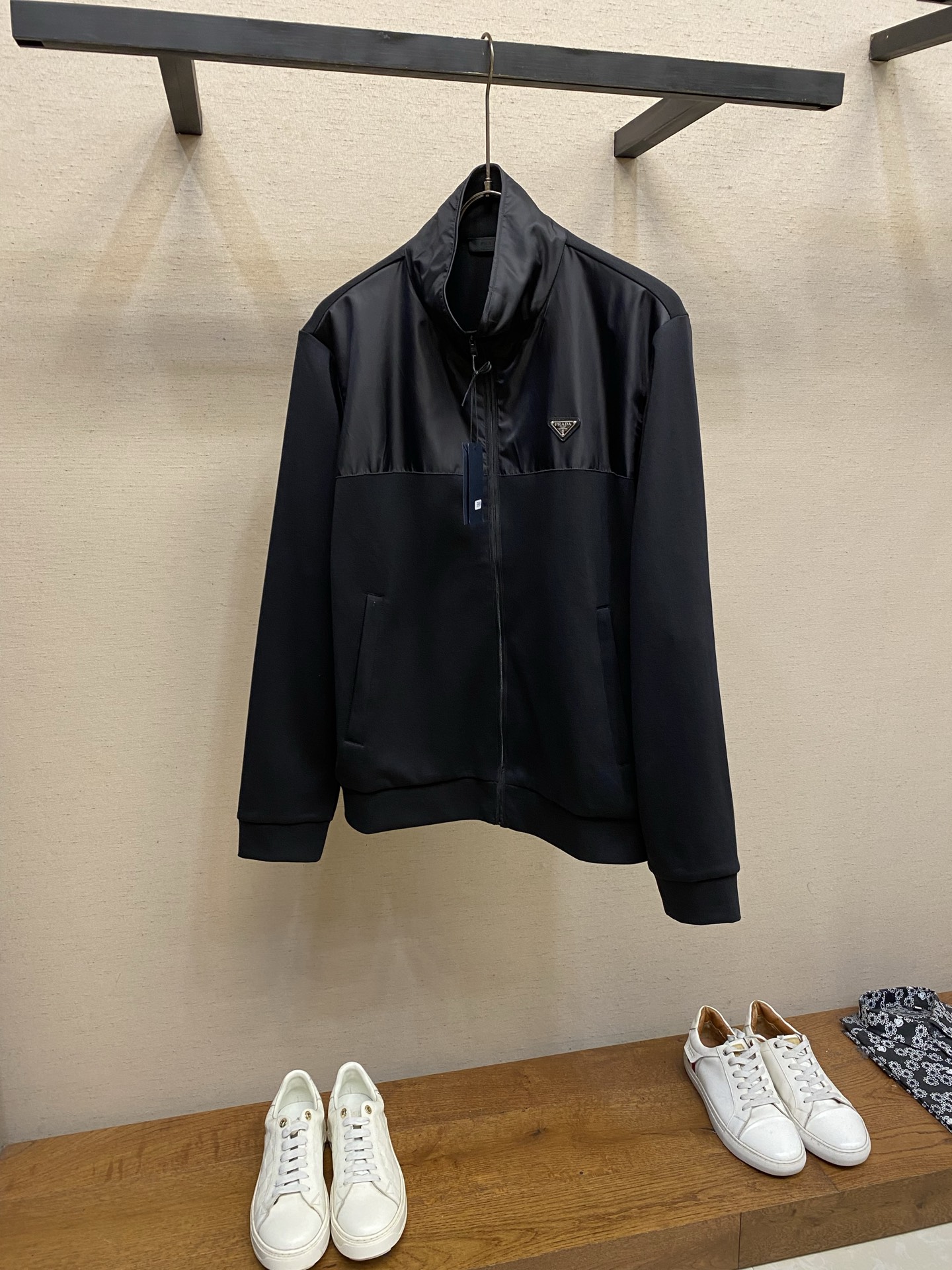 NO:947048,Prada, Cotton paneled nylon jacket Fabric options  Dual-material segmented splicing is used. The stand-up collar and placket areas are made of high-density nylon fabric. The body, sleeves, hem, etc. are made of cotton knitted fabric. The nylon surface layer is made of high-density plain weave technology. The cloth surface has a delicate matte luster. The yarn is tight and tear-resistant, and is stain-resistant and easy to wipe.  , it is stiff and not easy to wrinkle after being set, and it maintains a flat shape after being worn for a long time; the cotton knitted main body is woven with high-elastic cotton blended yarn, the fine knitted texture is soft and skin-friendly, with sufficient breathable pores, it can wick away perspiration during daily activities without being stuffy, it has a soft drape feeling, moderate elasticity and is not tight.  (Both fabrics have been pre-shrunk, color-fixed and washed, and the shrinkage rate is uniform at the splicing points. Long-term wear will not cause length misalignment, whitening or fading.) Segmented alignment splicing process  The pieces are pre-divided and cut, and the nylon pieces on the neckline and front chest are accurately aligned with the cotton body. Double-layer overlocking is used at the splicing. The outer double-threaded open thread is evenly reinforced. The stitch length is uniform and regular, which disperses the pulling force at the splicing area, greatly reducing the problems of thread breakage and layering warping during wearing and washing. There are no burrs inside and outside, and the splicing lines are smooth and smooth. Details  1. The one-piece stand-up collar is sewn with double-layer nylon panels. The collar has multiple parallel open-stitched lines to shape the collar, which is not easy to collapse and roll over. The middle is a customized metal nylon full-width zipper with a die-cast letter logo on the zipper head. The teeth bite smoothly without jamming. Double-layer fabric wrapping and reinforcement on both sides of the zipper prevents the thread from collapsing after repeated pulling. The zipper track is straight and neat.  2. Zipper pockets are inserted diagonally on both sides, with double-layer composite lock seams on the bag, and invisible zippers of the same color. The edges of the bag are reinforced with threads to prevent deformation and cracking when pulled. 3. The cuffs and hem are made of high-elastic cotton rib knitting of the same color, with double-layer folding and sewing. The elasticity lasts and is not easy to loosen and deform. It fits the wrists and waist without being tight. It is windproof and temperature-locking during exercise. The bends are wear-resistant and pill-resistant, and the edges will not loosen after repeated washing.  Sizes S-XL,,prada,jackets & coats,19860909Prada,,棉质拼接尼龙外套  面料选择 采用双材质分段拼接,立领、门襟区域为高密尼龙面料,衣身、袖子、下摆等选用棉质针织面料.尼龙面层采用高密平纹梭织工艺,布面自带细腻哑光光泽,纱线紧实抗撕裂,且耐脏易擦拭,定型后挺括不易起皱,长久穿着保持平整版型；棉质针织主体选用高弹棉混纺纱线织造,细密针织肌理柔软亲肤,透气孔隙充足,日常活动排汗不闷身,自带柔和垂坠感,弹力适中不紧绷. (两种面料均经过预缩、固色水洗后整理,拼接处收缩率统一,长期穿着不会出现长短错位、发白掉色问题)  分段对位拼接工艺 裁片预先分区分料裁剪,领口、前胸尼龙裁片与棉质衣身精准对位,拼接处采用双层包缝锁边,外层双道明线均匀加固,针距统一规整,分散拼接处拉扯受力,大幅度降低穿洗断线、分层起翘问题,里外无毛边毛刺,拼接线条流畅平整. 细节 1、一体式立领采用双层尼龙裁片复合缝制,领口多道平行明线定型,不易软塌翻卷；中间定制金属尼龙全幅拉链,拉链头压铸字母标识,齿牙咬合顺滑不卡顿,拉链两侧双层布料包边加固,反复拉合不易崩线,拉链轨道走线平直工整. 2、两侧斜插拉链口袋,袋片双层复合锁缝,搭配同色系隐形拉链,袋口四周满线加固,拉扯不易变形开裂. 3袖口、下摆采用高弹同色系棉质罗纹针织,双层对折车缝,弹力持久不易松弛变形,贴合手腕、腰腹不紧绷,运动时防风锁温,弯折处耐磨抗起球,多次洗涤不松垮卷边. 尺码S-XL,,prada,jackets & coats,,Men's clothing