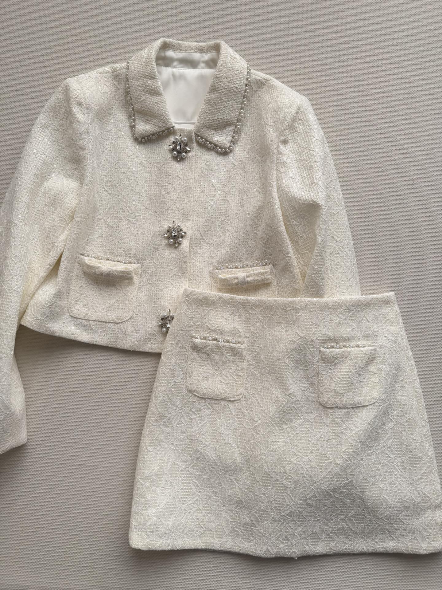 NO:715206,MAI DIRE MAI*26SS's small fragrant suit with pearl diamond buttons is made of cream apricot tweed. The lace fabric has a delicate and layered texture. The pearl lapel + diamond button design is retro and gorgeous, with full details. The short tailoring modifies the body shape, and it is super elegant when paired with a high-waist skirt. The pocket bow embellishment is soft and romantic, a must-have for spring lady style. It can be easily used for commuting or formal occasions. This set is practical and fashionable!  SML,,skirts,19860909MAI DIRE MAI*26SS的珍珠钻扣小香风套装,采用奶油杏色粗花呢,蕾丝面料质感细腻有层次.珍珠翻领+钻扣设计,复古又华丽,细节满分骨.短款剪裁修饰身形,搭配高腰半裙超显优雅气质.口袋蝴蝶结点缀,柔美浪漫,春日名媛风必备,通勤或正式场合都能轻松驾驭,一套实用又时髦！SML,,skirts,,Women's clothing