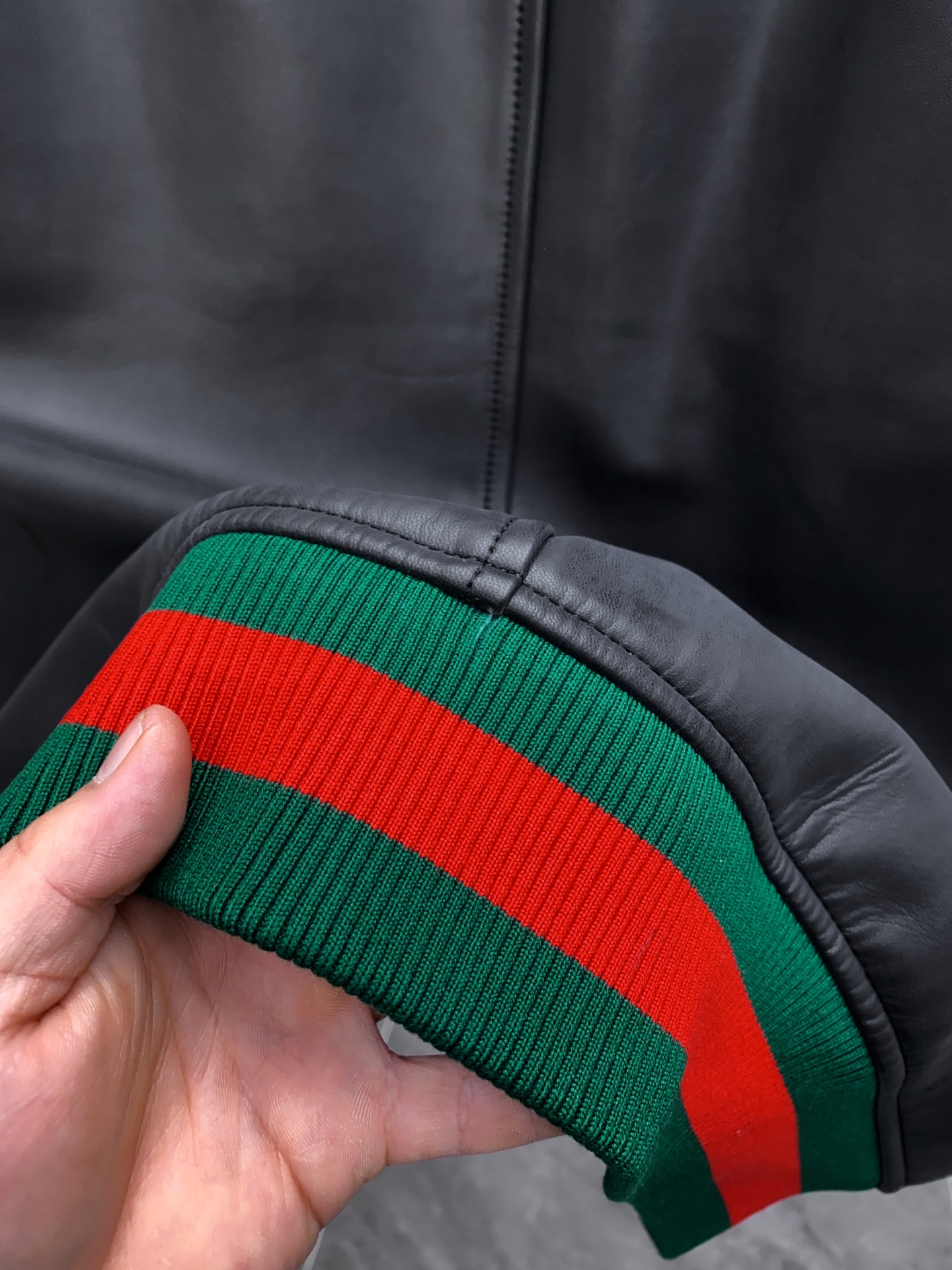 P1260 Gucci古驰纳帕皮飞行员夹克外套 。柔软纳帕皮革 + 羊毛棉混纺针织,质感与舒适度
外层选用柔软细腻的黑色纳帕羊皮,皮质纹理自然细腻,触感顺滑,兼具挺括感与柔韧度。表面光泽均匀,展现低调奢华的高级质感。 
针织拼接工艺 袖子与背部采用羊毛与棉混纺针织面料,针脚密实且富有弹性。在保持舒适穿着体验的同时,增强衣身的透气性与灵活性。立体剪裁版型直筒修身飞行员夹克版型,肩线挺括,身形利落。拼接工艺自然过渡 兼顾运动风与都市感。
门襟配备金属拉链,顺滑耐用。 袖口与下摆采用罗纹针织,并点缀 经典红绿织带,彰显标志性元素。 内里采用光滑里布拼接针织,穿着顺滑舒适。增添保暖性与耐穿性。