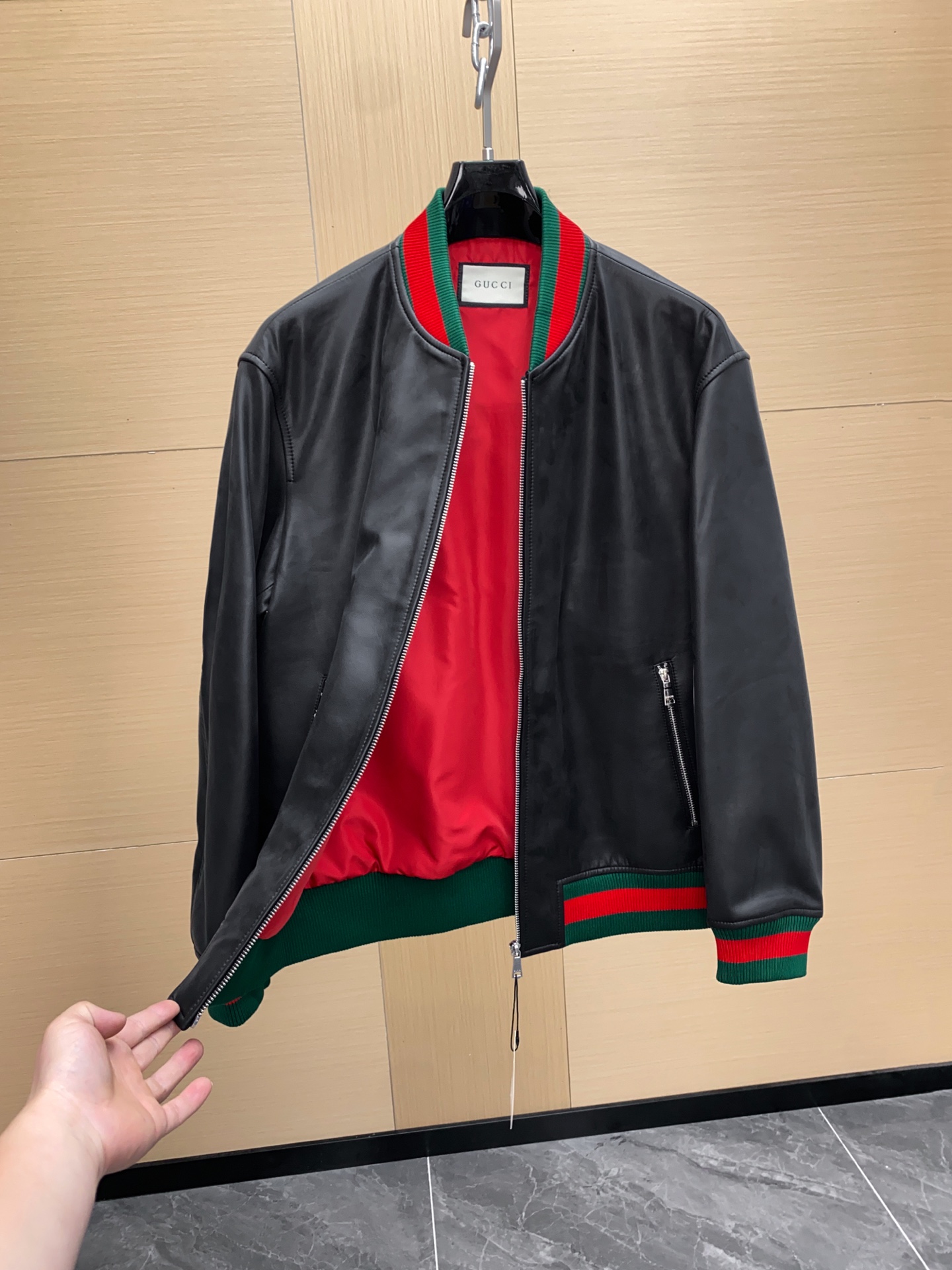 P1260 Gucci古驰纳帕皮飞行员夹克外套 。柔软纳帕皮革 + 羊毛棉混纺针织,质感与舒适度
外层选用柔软细腻的黑色纳帕羊皮,皮质纹理自然细腻,触感顺滑,兼具挺括感与柔韧度。表面光泽均匀,展现低调奢华的高级质感。 
针织拼接工艺 袖子与背部采用羊毛与棉混纺针织面料,针脚密实且富有弹性。在保持舒适穿着体验的同时,增强衣身的透气性与灵活性。立体剪裁版型直筒修身飞行员夹克版型,肩线挺括,身形利落。拼接工艺自然过渡 兼顾运动风与都市感。
门襟配备金属拉链,顺滑耐用。 袖口与下摆采用罗纹针织,并点缀 经典红绿织带,彰显标志性元素。 内里采用光滑里布拼接针织,穿着顺滑舒适。增添保暖性与耐穿性。