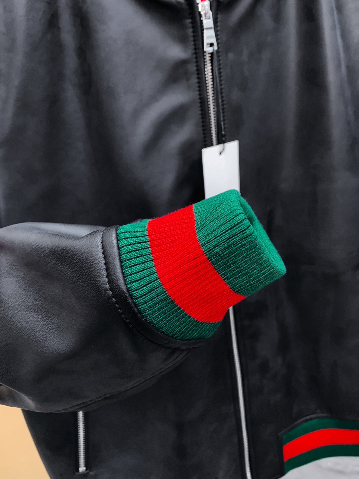 P1260 Gucci古驰纳帕皮飞行员夹克外套 。柔软纳帕皮革 + 羊毛棉混纺针织,质感与舒适度
外层选用柔软细腻的黑色纳帕羊皮,皮质纹理自然细腻,触感顺滑,兼具挺括感与柔韧度。表面光泽均匀,展现低调奢华的高级质感。 
针织拼接工艺 袖子与背部采用羊毛与棉混纺针织面料,针脚密实且富有弹性。在保持舒适穿着体验的同时,增强衣身的透气性与灵活性。立体剪裁版型直筒修身飞行员夹克版型,肩线挺括,身形利落。拼接工艺自然过渡 兼顾运动风与都市感。
门襟配备金属拉链,顺滑耐用。 袖口与下摆采用罗纹针织,并点缀 经典红绿织带,彰显标志性元素。 内里采用光滑里布拼接针织,穿着顺滑舒适。增添保暖性与耐穿性。