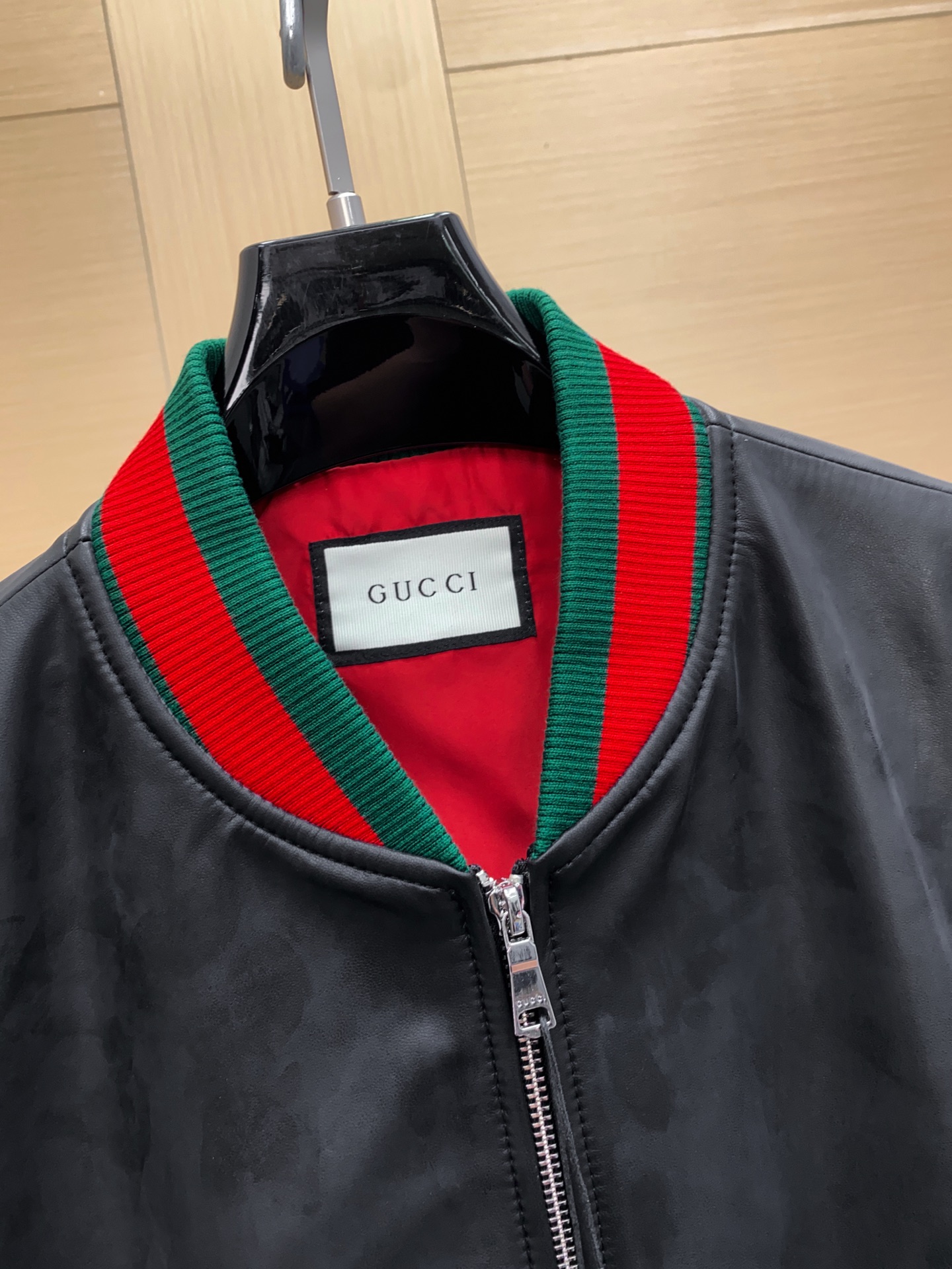 P1260 Gucci古驰纳帕皮飞行员夹克外套 。柔软纳帕皮革 + 羊毛棉混纺针织,质感与舒适度
外层选用柔软细腻的黑色纳帕羊皮,皮质纹理自然细腻,触感顺滑,兼具挺括感与柔韧度。表面光泽均匀,展现低调奢华的高级质感。 
针织拼接工艺 袖子与背部采用羊毛与棉混纺针织面料,针脚密实且富有弹性。在保持舒适穿着体验的同时,增强衣身的透气性与灵活性。立体剪裁版型直筒修身飞行员夹克版型,肩线挺括,身形利落。拼接工艺自然过渡 兼顾运动风与都市感。
门襟配备金属拉链,顺滑耐用。 袖口与下摆采用罗纹针织,并点缀 经典红绿织带,彰显标志性元素。 内里采用光滑里布拼接针织,穿着顺滑舒适。增添保暖性与耐穿性。