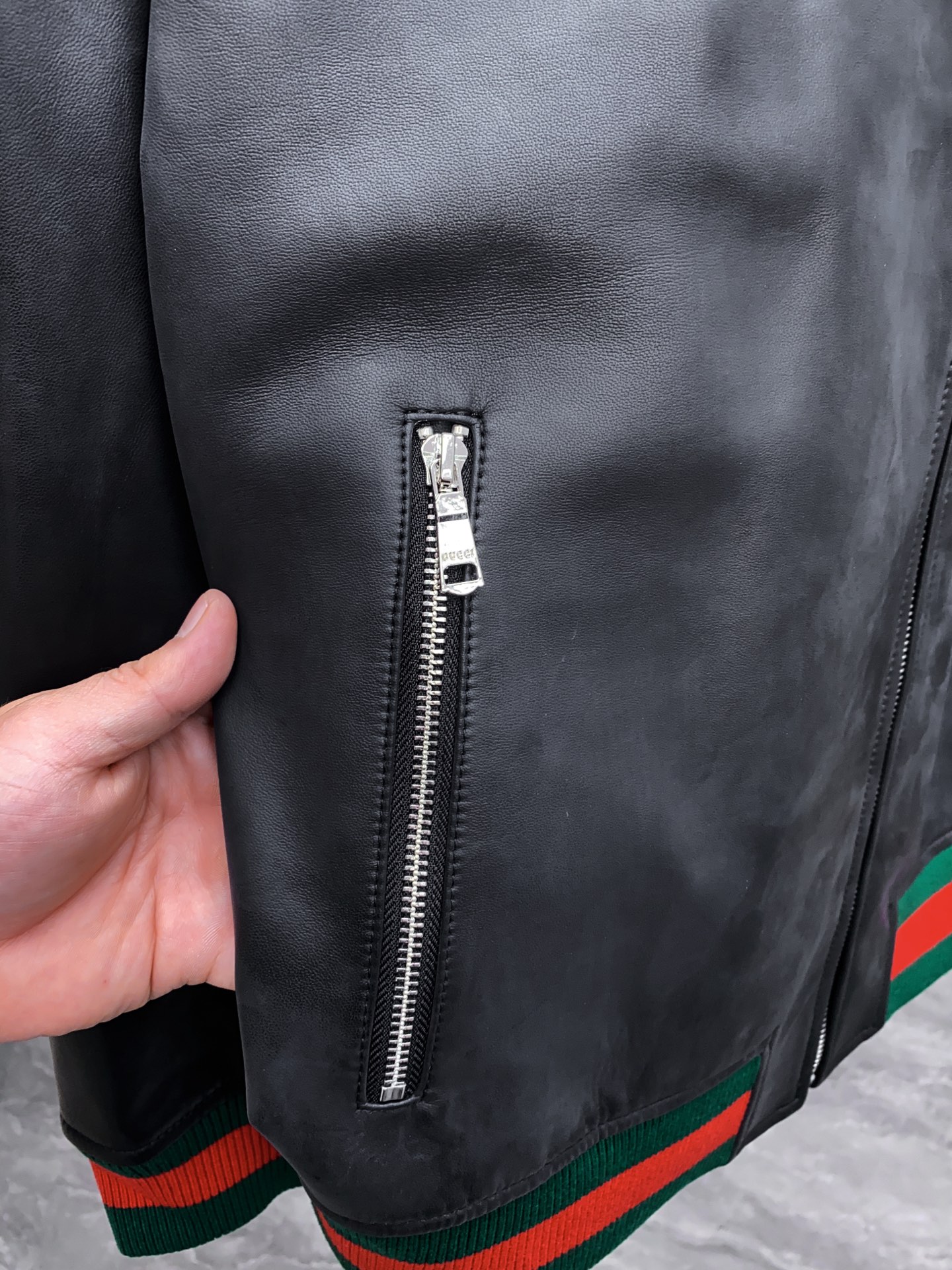 P1260 Gucci古驰纳帕皮飞行员夹克外套 。柔软纳帕皮革 + 羊毛棉混纺针织,质感与舒适度
外层选用柔软细腻的黑色纳帕羊皮,皮质纹理自然细腻,触感顺滑,兼具挺括感与柔韧度。表面光泽均匀,展现低调奢华的高级质感。 
针织拼接工艺 袖子与背部采用羊毛与棉混纺针织面料,针脚密实且富有弹性。在保持舒适穿着体验的同时,增强衣身的透气性与灵活性。立体剪裁版型直筒修身飞行员夹克版型,肩线挺括,身形利落。拼接工艺自然过渡 兼顾运动风与都市感。
门襟配备金属拉链,顺滑耐用。 袖口与下摆采用罗纹针织,并点缀 经典红绿织带,彰显标志性元素。 内里采用光滑里布拼接针织,穿着顺滑舒适。增添保暖性与耐穿性。