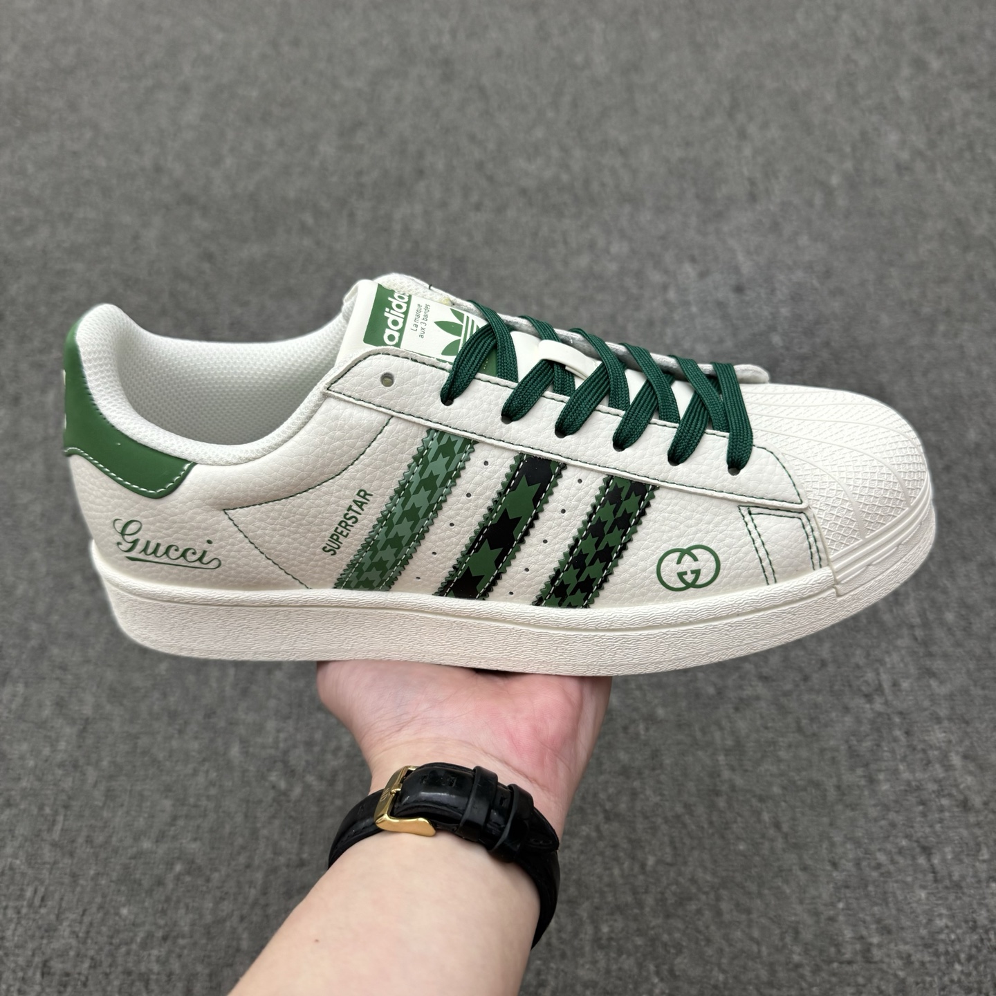 双十一特价福利得 (36-45半) 公司级 头层 [定制球鞋] Gucci x Adidas Original Superstar 古驰古奇 x 阿迪达斯 低帮 联名米白绿 贝壳头防滑耐磨轻便低邦板鞋男女同款 鞋身整体采用米白色皮革打造,搭配经典米白贝壳头,鞋身两侧经典锯齿三条杠Logo采用绿色点缀,侧身Superstar字样辅以绿色压印妆点,鞋舌上以Adidas字样及三叶草Logo呈现,瞬间提升鞋子的时尚程度,后跟装饰片辅以绿色皮革制作并带有白色Adidas字样及三叶草Logoq,后跟印有Gucci字样,彰显联名身份;最后以米白色中底搭配同色橡胶外底完善整体设计收尾. 货号:DS0022