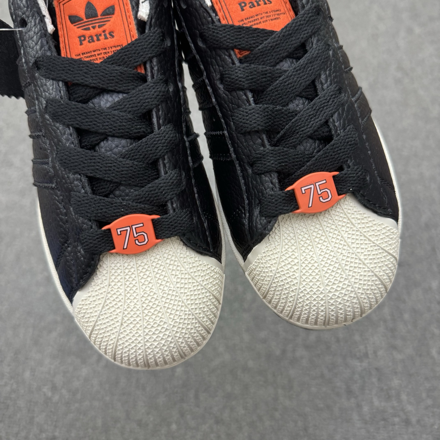 【💰💰110】（35.5-45半）
Adidas Original Superstar 2 "Paris" 阿迪达斯 低帮 巴黎联名 黑橙 男女同款 贝壳头2代防滑耐磨轻便低邦板鞋 鞋身整体以黑色皮革打造，搭配经典白色贝壳头，鞋身两侧经典锯齿三条杠Logo采用黑色点缀，侧身Superstar字样橙色压印妆点，鞋舌橙色底色上以三叶草Logo及Paris字样呈现，瞬间提升鞋子的时尚程度，后跟装饰片辅以黑色皮革制作并带有白色三叶草Logo及Paris字样，外加法国75数字的鞋带饰品致敬巴黎区号，最后以白色中底搭配生胶色橡胶外底完善整体设计收尾。
货号：JQ3223
尺码：35¹/₃ 36 36²/₃ 37¹/₃ 38 38²/₃ 39¹/₃ 40 40²/₃ 41¹/₃ 42 42²/₃ 43¹/₃ 44 44²/₃ 45¹/₃