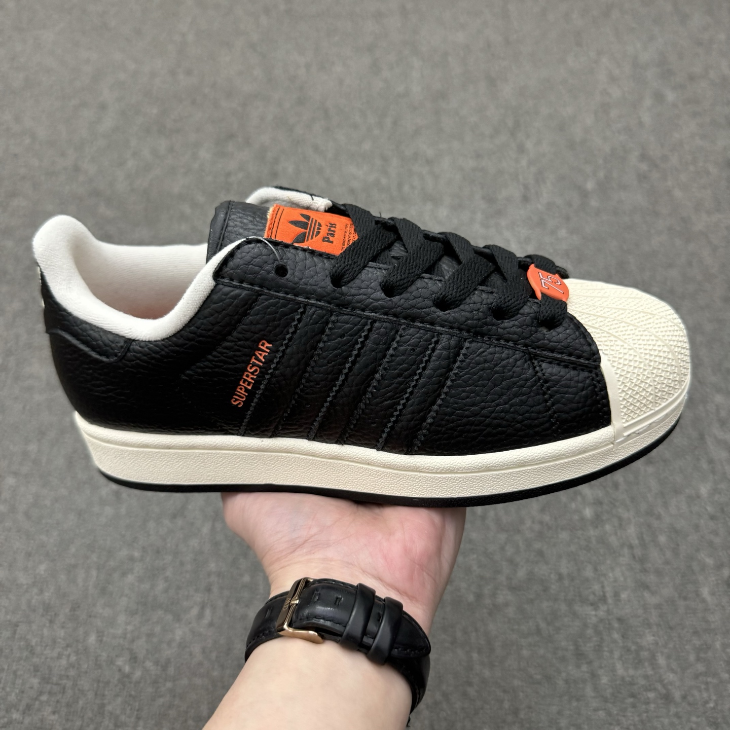 【💰💰110】（35.5-45半）
Adidas Original Superstar 2 "Paris" 阿迪达斯 低帮 巴黎联名 黑橙 男女同款 贝壳头2代防滑耐磨轻便低邦板鞋 鞋身整体以黑色皮革打造，搭配经典白色贝壳头，鞋身两侧经典锯齿三条杠Logo采用黑色点缀，侧身Superstar字样橙色压印妆点，鞋舌橙色底色上以三叶草Logo及Paris字样呈现，瞬间提升鞋子的时尚程度，后跟装饰片辅以黑色皮革制作并带有白色三叶草Logo及Paris字样，外加法国75数字的鞋带饰品致敬巴黎区号，最后以白色中底搭配生胶色橡胶外底完善整体设计收尾。
货号：JQ3223
尺码：35¹/₃ 36 36²/₃ 37¹/₃ 38 38²/₃ 39¹/₃ 40 40²/₃ 41¹/₃ 42 42²/₃ 43¹/₃ 44 44²/₃ 45¹/₃