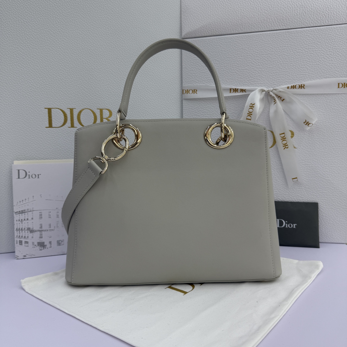 Dior 2026蝴蝶结手提包_编号7038_云雾灰金扣
🎀 Dior 2026 春夏新品#蝴蝶结手提包「云雾灰色」
新设计的轮廓与造型，配色 丰富，适配多人！在夸张与优雅之间恰到好处！它的设计灵感源于迪奥先生设计的 Cigale礼服~立体的梯形包身+单手柄，造型自带优雅大气的腔调。包包的外观比较低调，几乎没有什么明显的大Logo。离近点再看，才发现原来Anderson把Dior字母Logo和包包提手的圆孔融合到了一起。
包包既有辨识度，也完全不是张扬挂的，整体散发着那种不动声色的高级感！值得一提的是，这款包还搭配了一条皮质长肩带。尤其出门旅行的时候就可以换上长肩带，既解放了双手，还衬得人轻松又随性~
型号：7038
尺寸：28*10*22（长*宽*高）