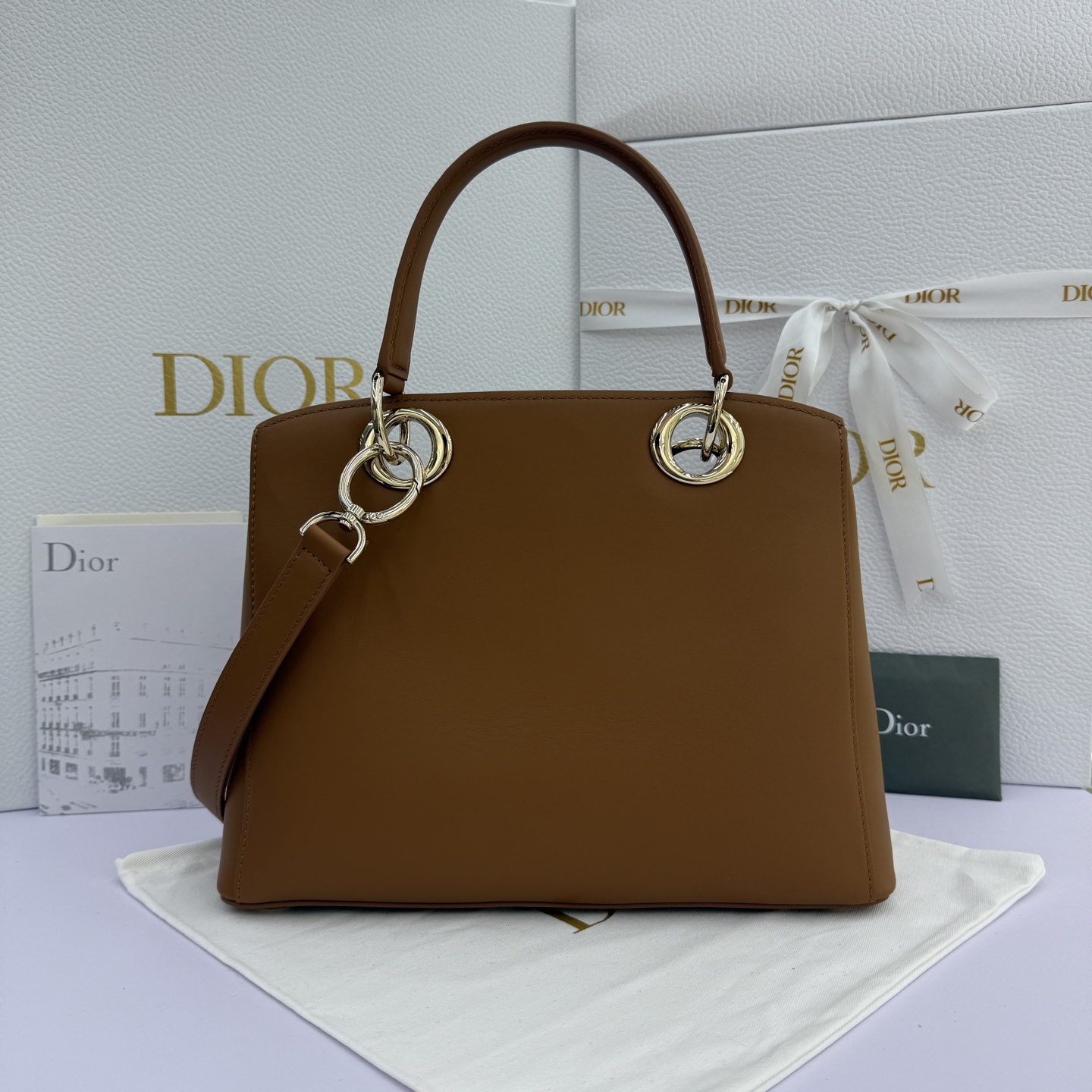 Dior 2026蝴蝶结手提包_编号7038_焦糖色金扣
🎀 Dior 2026 春夏新品#蝴蝶结手提包「焦糖色」
新设计的轮廓与造型，配色 丰富，适配多人！在夸张与优雅之间恰到好处！它的设计灵感源于迪奥先生设计的 Cigale礼服~立体的梯形包身+单手柄，造型自带优雅大气的腔调。包包的外观比较低调，几乎没有什么明显的大Logo。离近点再看，才发现原来Anderson把Dior字母Logo和包包提手的圆孔融合到了一起。
包包既有辨识度，也完全不是张扬挂的，整体散发着那种不动声色的高级感！值得一提的是，这款包还搭配了一条皮质长肩带。尤其出门旅行的时候就可以换上长肩带，既解放了双手，还衬得人轻松又随性~
型号：7038
尺寸：28*10*22（长*宽*高）