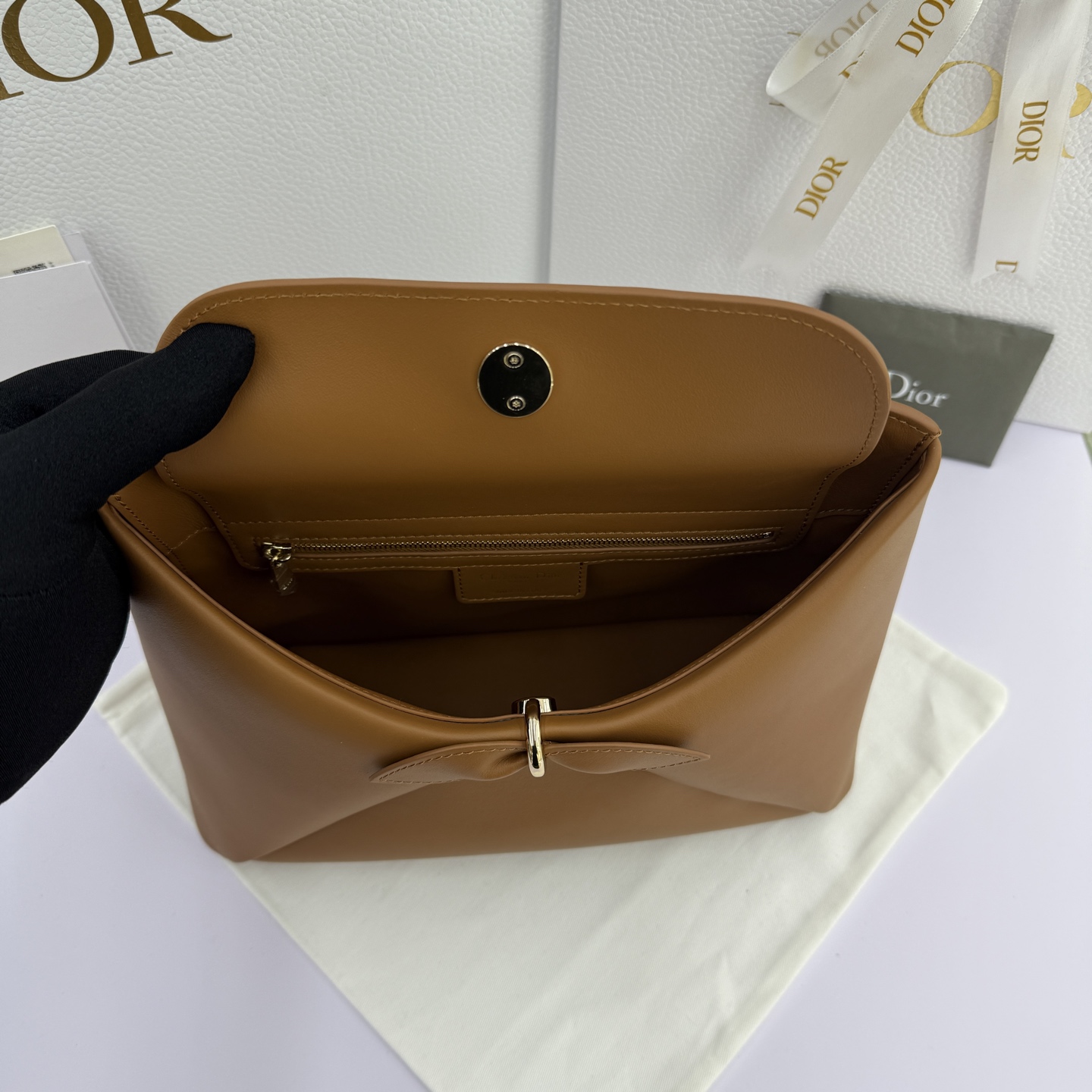 Dior 2026蝴蝶结手提包_编号7038_焦糖色金扣
🎀 Dior 2026 春夏新品#蝴蝶结手提包「焦糖色」
新设计的轮廓与造型，配色 丰富，适配多人！在夸张与优雅之间恰到好处！它的设计灵感源于迪奥先生设计的 Cigale礼服~立体的梯形包身+单手柄，造型自带优雅大气的腔调。包包的外观比较低调，几乎没有什么明显的大Logo。离近点再看，才发现原来Anderson把Dior字母Logo和包包提手的圆孔融合到了一起。
包包既有辨识度，也完全不是张扬挂的，整体散发着那种不动声色的高级感！值得一提的是，这款包还搭配了一条皮质长肩带。尤其出门旅行的时候就可以换上长肩带，既解放了双手，还衬得人轻松又随性~
型号：7038
尺寸：28*10*22（长*宽*高）