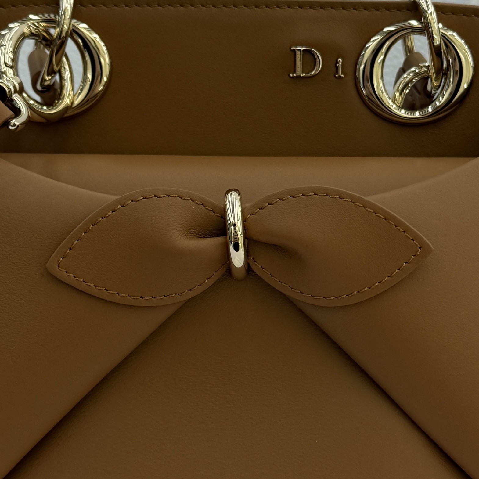 Dior 2026蝴蝶结手提包_编号7038_焦糖色金扣
🎀 Dior 2026 春夏新品#蝴蝶结手提包「焦糖色」
新设计的轮廓与造型，配色 丰富，适配多人！在夸张与优雅之间恰到好处！它的设计灵感源于迪奥先生设计的 Cigale礼服~立体的梯形包身+单手柄，造型自带优雅大气的腔调。包包的外观比较低调，几乎没有什么明显的大Logo。离近点再看，才发现原来Anderson把Dior字母Logo和包包提手的圆孔融合到了一起。
包包既有辨识度，也完全不是张扬挂的，整体散发着那种不动声色的高级感！值得一提的是，这款包还搭配了一条皮质长肩带。尤其出门旅行的时候就可以换上长肩带，既解放了双手，还衬得人轻松又随性~
型号：7038
尺寸：28*10*22（长*宽*高）