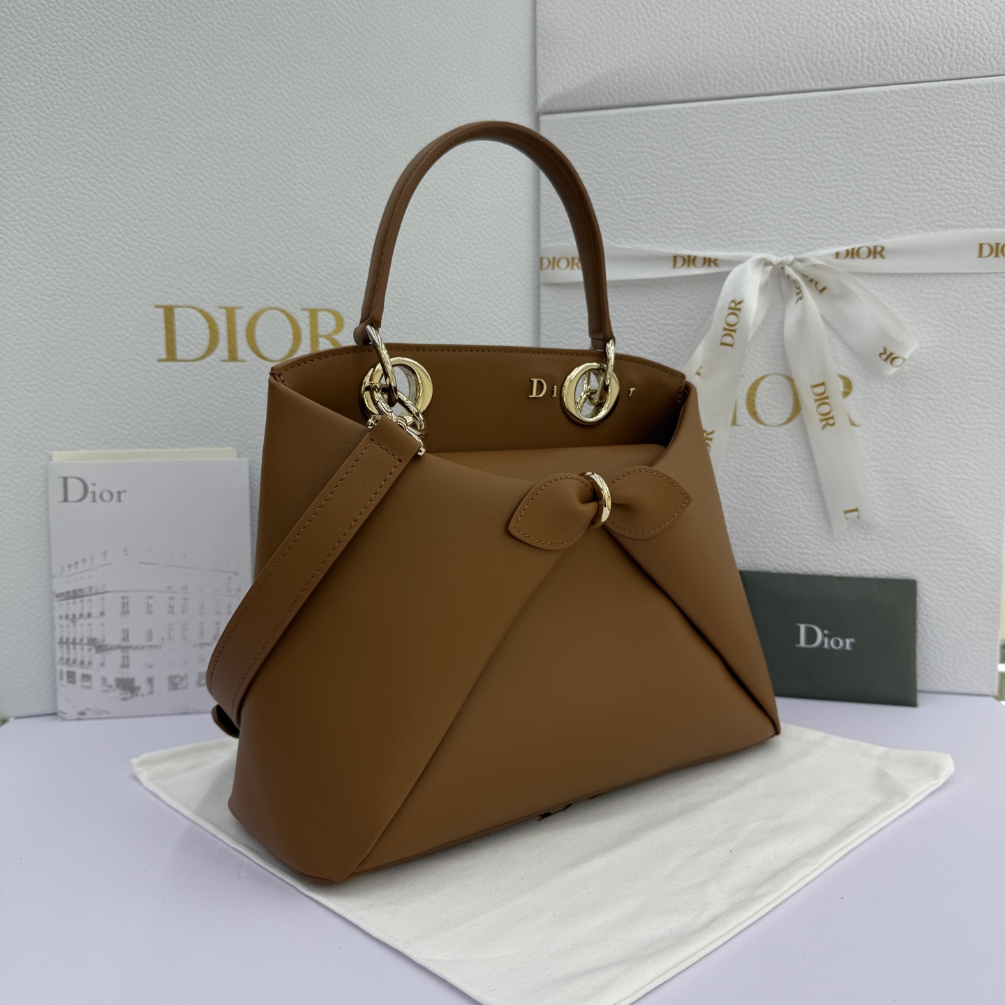 Dior 2026蝴蝶结手提包_编号7038_焦糖色金扣
🎀 Dior 2026 春夏新品#蝴蝶结手提包「焦糖色」
新设计的轮廓与造型，配色 丰富，适配多人！在夸张与优雅之间恰到好处！它的设计灵感源于迪奥先生设计的 Cigale礼服~立体的梯形包身+单手柄，造型自带优雅大气的腔调。包包的外观比较低调，几乎没有什么明显的大Logo。离近点再看，才发现原来Anderson把Dior字母Logo和包包提手的圆孔融合到了一起。
包包既有辨识度，也完全不是张扬挂的，整体散发着那种不动声色的高级感！值得一提的是，这款包还搭配了一条皮质长肩带。尤其出门旅行的时候就可以换上长肩带，既解放了双手，还衬得人轻松又随性~
型号：7038
尺寸：28*10*22（长*宽*高）