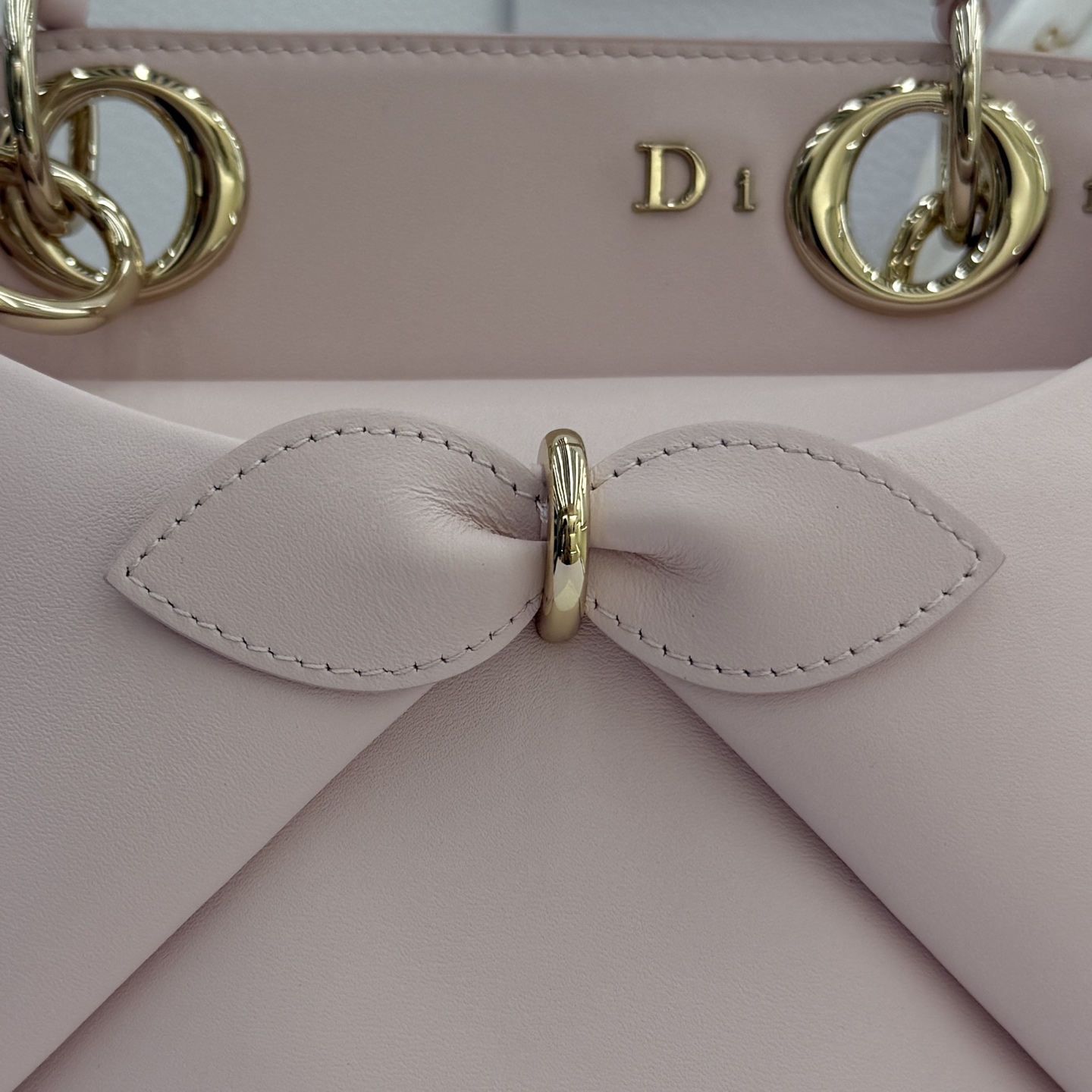 Dior 2026蝴蝶结手提包_编号7038_淡粉色金扣
🎀 Dior 2026 春夏新品#蝴蝶结手提包「淡粉色」
新设计的轮廓与造型，配色 丰富，适配多人！在夸张与优雅之间恰到好处！它的设计灵感源于迪奥先生设计的 Cigale礼服~立体的梯形包身+单手柄，造型自带优雅大气的腔调。包包的外观比较低调，几乎没有什么明显的大Logo。离近点再看，才发现原来Anderson把Dior字母Logo和包包提手的圆孔融合到了一起。
包包既有辨识度，也完全不是张扬挂的，整体散发着那种不动声色的高级感！值得一提的是，这款包还搭配了一条皮质长肩带。尤其出门旅行的时候就可以换上长肩带，既解放了双手，还衬得人轻松又随性~
型号：7038
尺寸：28*10*22（长*宽*高）