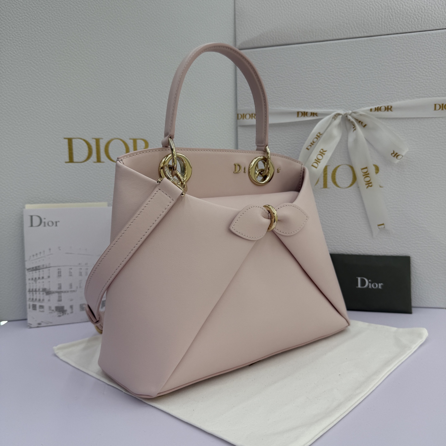 Dior 2026蝴蝶结手提包_编号7038_淡粉色金扣
🎀 Dior 2026 春夏新品#蝴蝶结手提包「淡粉色」
新设计的轮廓与造型，配色 丰富，适配多人！在夸张与优雅之间恰到好处！它的设计灵感源于迪奥先生设计的 Cigale礼服~立体的梯形包身+单手柄，造型自带优雅大气的腔调。包包的外观比较低调，几乎没有什么明显的大Logo。离近点再看，才发现原来Anderson把Dior字母Logo和包包提手的圆孔融合到了一起。
包包既有辨识度，也完全不是张扬挂的，整体散发着那种不动声色的高级感！值得一提的是，这款包还搭配了一条皮质长肩带。尤其出门旅行的时候就可以换上长肩带，既解放了双手，还衬得人轻松又随性~
型号：7038
尺寸：28*10*22（长*宽*高）