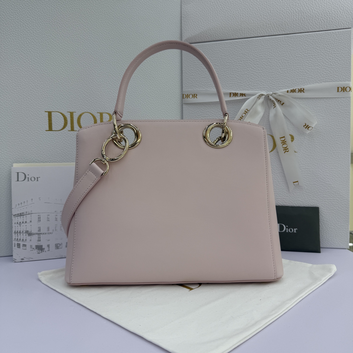 Dior 2026蝴蝶结手提包_编号7038_淡粉色金扣
🎀 Dior 2026 春夏新品#蝴蝶结手提包「淡粉色」
新设计的轮廓与造型，配色 丰富，适配多人！在夸张与优雅之间恰到好处！它的设计灵感源于迪奥先生设计的 Cigale礼服~立体的梯形包身+单手柄，造型自带优雅大气的腔调。包包的外观比较低调，几乎没有什么明显的大Logo。离近点再看，才发现原来Anderson把Dior字母Logo和包包提手的圆孔融合到了一起。
包包既有辨识度，也完全不是张扬挂的，整体散发着那种不动声色的高级感！值得一提的是，这款包还搭配了一条皮质长肩带。尤其出门旅行的时候就可以换上长肩带，既解放了双手，还衬得人轻松又随性~
型号：7038
尺寸：28*10*22（长*宽*高）