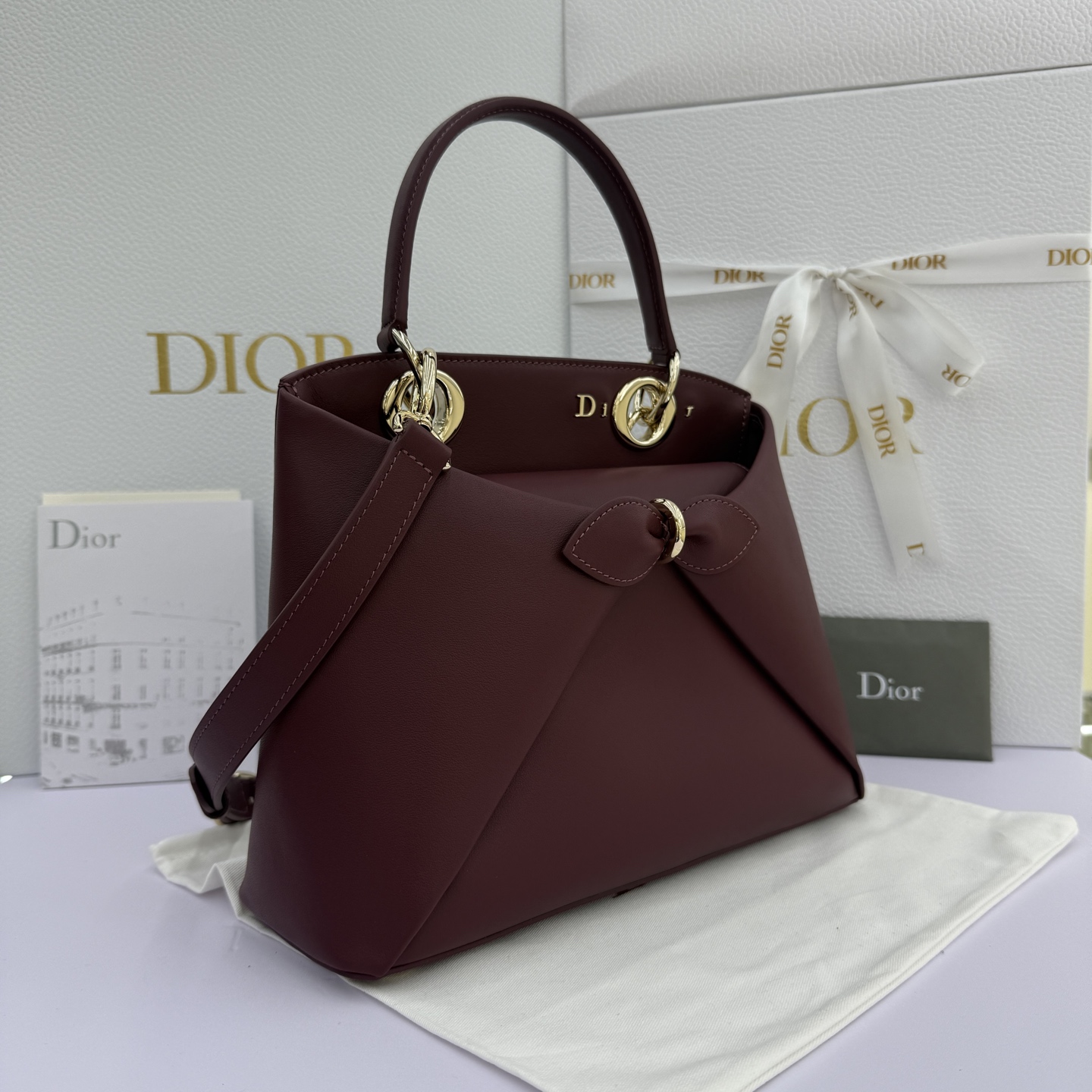 Dior 2026蝴蝶结手提包_编号7038_酒红色金扣
🎀 Dior 2026 春夏新品#蝴蝶结手提包「酒红色」
新设计的轮廓与造型，配色 丰富，适配多人！在夸张与优雅之间恰到好处！它的设计灵感源于迪奥先生设计的 Cigale礼服~立体的梯形包身+单手柄，造型自带优雅大气的腔调。包包的外观比较低调，几乎没有什么明显的大Logo。离近点再看，才发现原来Anderson把Dior字母Logo和包包提手的圆孔融合到了一起。
包包既有辨识度，也完全不是张扬挂的，整体散发着那种不动声色的高级感！值得一提的是，这款包还搭配了一条皮质长肩带。尤其出门旅行的时候就可以换上长肩带，既解放了双手，还衬得人轻松又随性~
型号：7038
尺寸：28*10*22（长*宽*高）