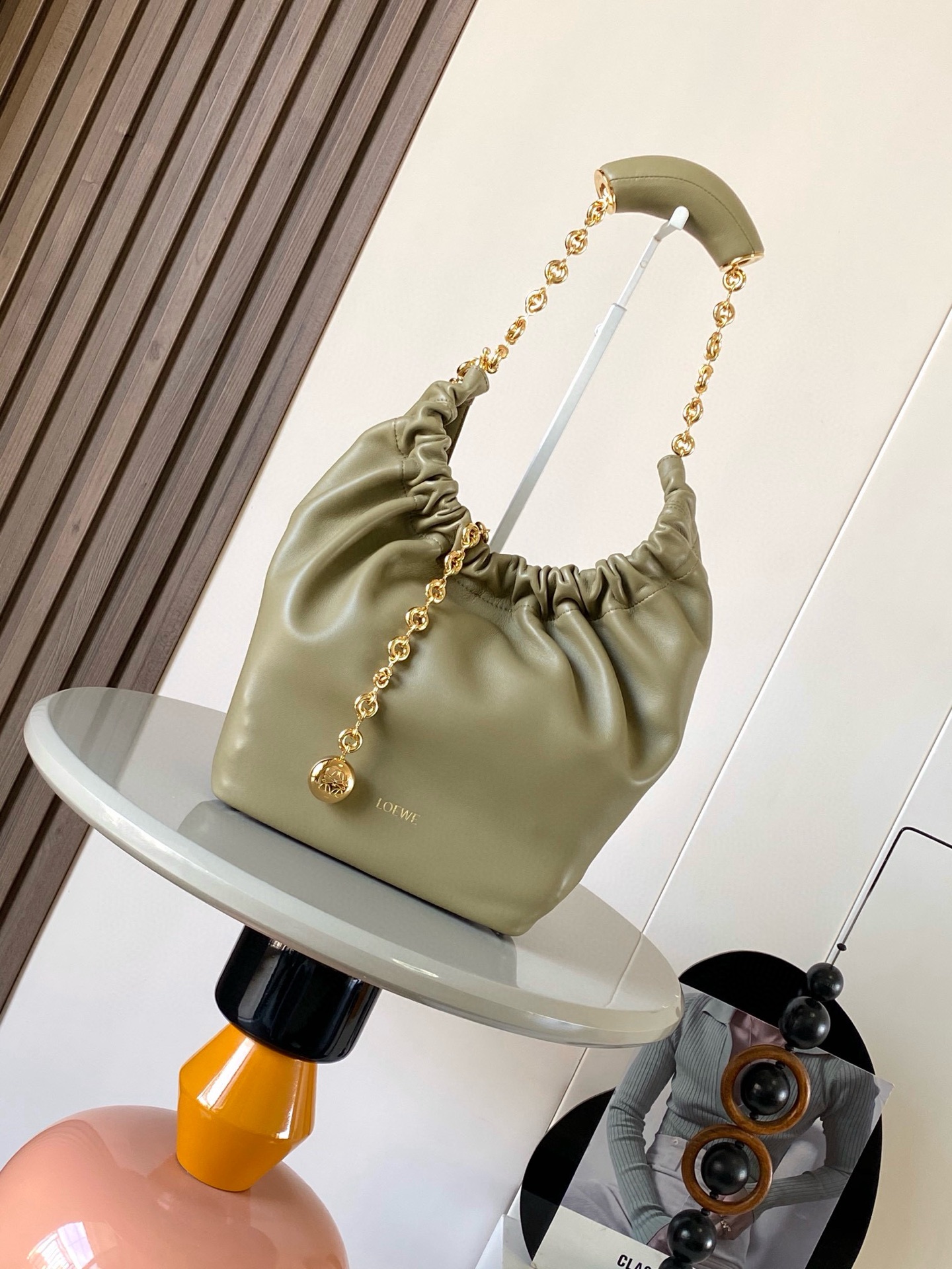 NO:209039,[Same Model for Celebrity] Small Napa Sheep Leather Squeeze Handbag is a new exquisite and soft handbag. The newly released Squeeze Handbag is made of soft and silky Mellow Napa Lambskin. The unlined structure effectively reduces the weight of the bag. It is also lighter. The meniscus shaped bag has an elegant ruffle closing, creating a relaxed and casual attitude. Another highlight of this bag is the ergonomic Squeeze airbag handle and exquisite donut chain made of brass. The length can be adjusted by chain ring or lengthening chain can be added, so that the airbag handles such as handcarrying, shoulders, crossbody, etc. can slide freely to improve comfort. The bottom of the chain is decorated with a piece of agile detail. Size 29CM~24CM~10.5CM.  Model number 9042 Color vetiver green, Loewe, sheepskin19860909【明星同款】小号纳帕羊皮革Squeeze手袋是款精致而柔美的全新手袋全新发布的 Squeeze 手袋采用柔软丝滑的Mellow纳帕小羊皮制作而成无衬里结构有效减轻包身自重观感上也更为轻盈弯月形包口以优雅的褶边收口,营造出轻松又随性的态度这款包包还有一大亮点是符合人体工程学的 Squeeze 气囊手柄搭配黄铜打造的精美甜甜圈链条可通过链环调节长短或添加延长链,实现手拎、肩背、斜挎等不同背法气囊手柄可自由滑动位置以提升舒适度链条底部点缀一枚 Anagram Pebble 吊坠为包包增添灵动细节 尺寸29CM～24CM～10.5CM 款号9042 颜色香根草绿,罗意威,loewe,sheepskin,Bag