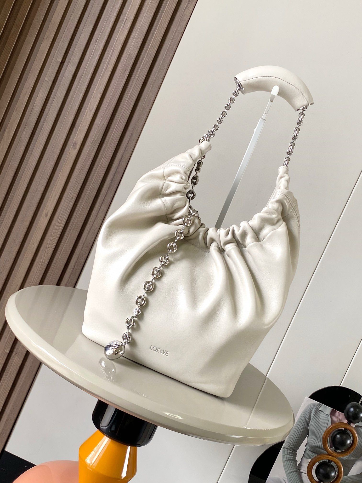 NO:209044,[Same Model for Celebrity] Small Napa Sheep Leather Squeeze Handbag is a new exquisite and soft handbag. The newly released Squeeze Handbag is made of soft and silky Mellow Napa Lambskin. The unlined structure effectively reduces the weight of the bag. It is also lighter. The meniscus shaped bag has an elegant ruffle closing, creating a relaxed and casual attitude. Another highlight of this bag is the ergonomic Squeeze airbag handle and exquisite donut chain made of brass. The length can be adjusted by chain ring or lengthening chain can be added, so that the airbag handles such as handcarrying, shoulders, crossbody, etc. can slide freely to improve comfort. The bottom of the chain is decorated with a piece of agile detail. Size 29CM~24CM~10.5CM.  Model number 9042 Color sea salt white, Luo Yiwei, loewe, sheepskin19860909【明星同款】小号纳帕羊皮革Squeeze手袋是款精致而柔美的全新手袋全新发布的 Squeeze 手袋采用柔软丝滑的Mellow纳帕小羊皮制作而成无衬里结构有效减轻包身自重观感上也更为轻盈弯月形包口以优雅的褶边收口,营造出轻松又随性的态度这款包包还有一大亮点是符合人体工程学的 Squeeze 气囊手柄搭配黄铜打造的精美甜甜圈链条可通过链环调节长短或添加延长链,实现手拎、肩背、斜挎等不同背法气囊手柄可自由滑动位置以提升舒适度链条底部点缀一枚 Anagram Pebble 吊坠为包包增添灵动细节 尺寸29CM～24CM～10.5CM 款号9042 颜色海盐白,罗意威,loewe,sheepskin,Bag