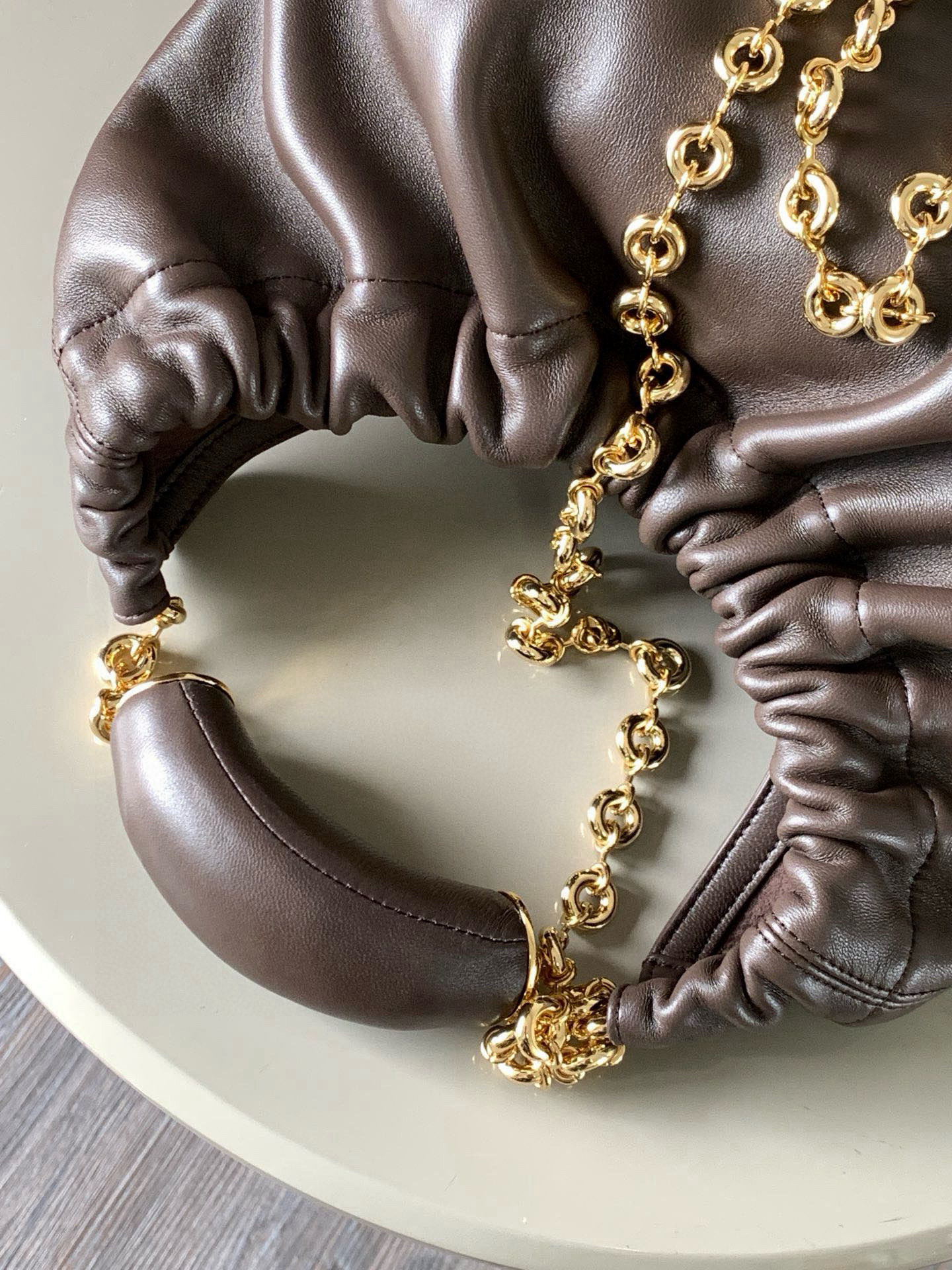 p980。🔥【明星同款】小号纳帕羊皮革Squeeze手袋💄是款精致而柔美的全新手袋💥全新发布的 Squeeze 手袋采用柔软丝滑的Mellow纳帕小羊皮制作而成❤️无衬里结构有效减轻包身自重🌺观感上也更为轻盈⭐️弯月形包口以优雅的褶边收口，营造出轻松又随性的态度👜这款包包还有一大亮点是符合人体工程学的 Squeeze 气囊手柄🌼搭配黄铜打造的精美甜甜圈链条😘可通过链环调节长短或添加延长链，实现手拎、肩背、斜挎等不同背法😻气囊手柄可自由滑动位置以提升舒适度🌻链条底部点缀一枚 Anagram Pebble 吊坠，为包包增添灵动细节⚡️
尺寸：29CM～24CM～10.5CM
款号：9042
颜色：巧克力