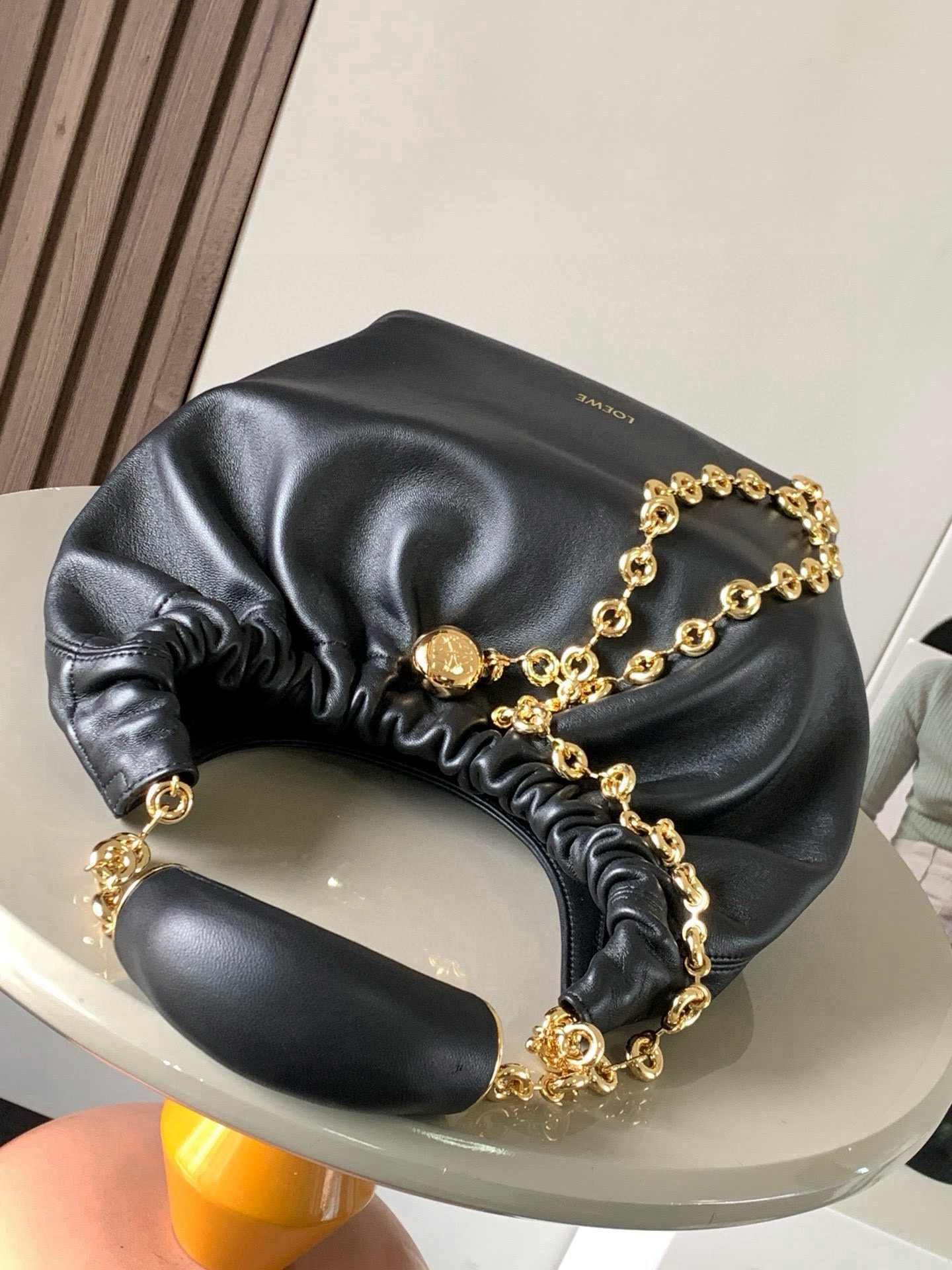 p980。🔥【明星同款】小号纳帕羊皮革Squeeze手袋💄是款精致而柔美的全新手袋💥全新发布的 Squeeze 手袋采用柔软丝滑的Mellow纳帕小羊皮制作而成❤️无衬里结构有效减轻包身自重🌺观感上也更为轻盈⭐️弯月形包口以优雅的褶边收口，营造出轻松又随性的态度👜这款包包还有一大亮点是符合人体工程学的 Squeeze 气囊手柄🌼搭配黄铜打造的精美甜甜圈链条😘可通过链环调节长短或添加延长链，实现手拎、肩背、斜挎等不同背法😻气囊手柄可自由滑动位置以提升舒适度🌻链条底部点缀一枚 Anagram Pebble 吊坠，为包包增添灵动细节⚡️
尺寸：29CM～24CM～10.5CM
款号：9042
颜色：黑色