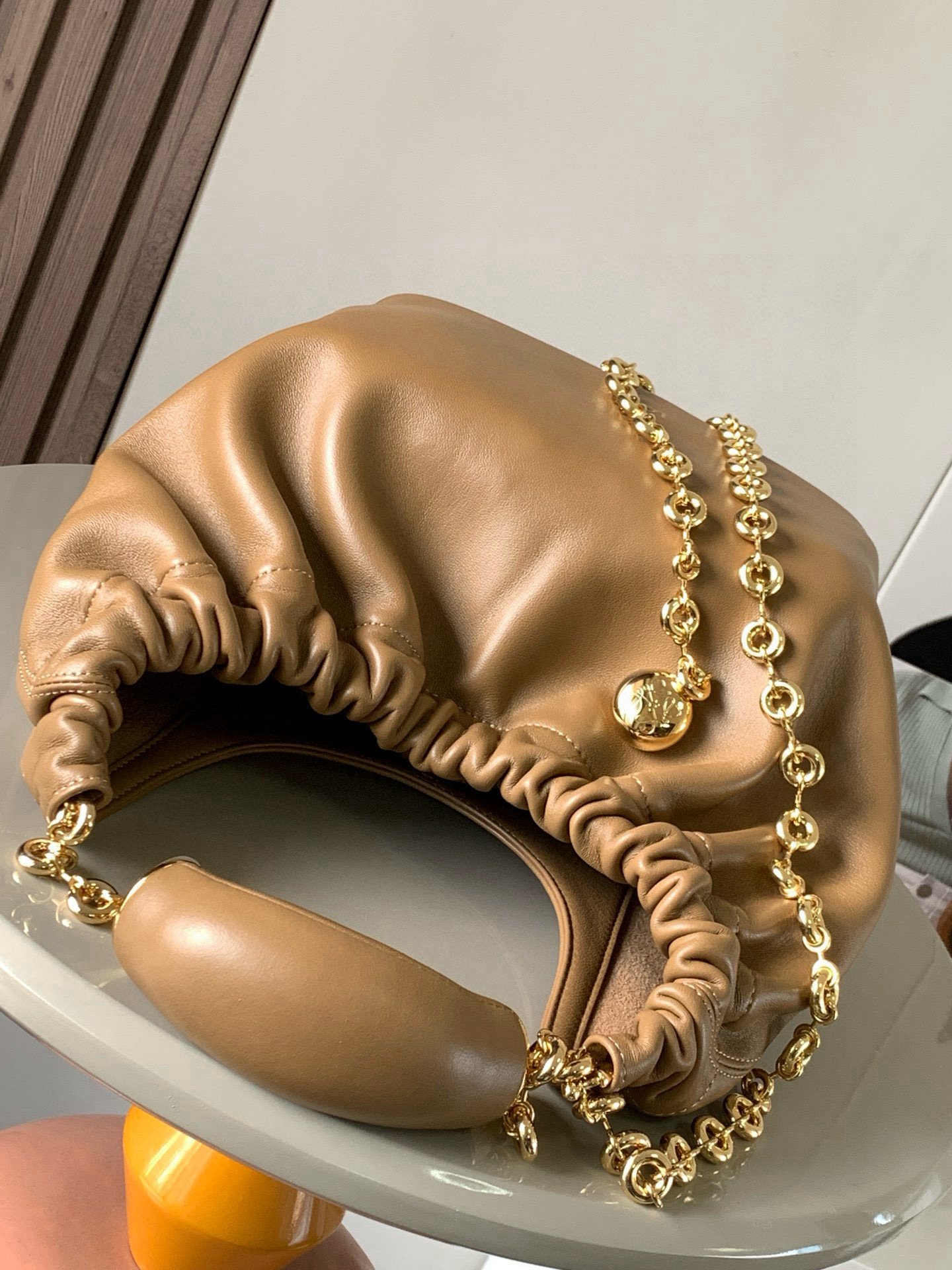 p980。🔥【明星同款】小号纳帕羊皮革Squeeze手袋💄是款精致而柔美的全新手袋💥全新发布的 Squeeze 手袋采用柔软丝滑的Mellow纳帕小羊皮制作而成❤️无衬里结构有效减轻包身自重🌺观感上也更为轻盈⭐️弯月形包口以优雅的褶边收口，营造出轻松又随性的态度👜这款包包还有一大亮点是符合人体工程学的 Squeeze 气囊手柄🌼搭配黄铜打造的精美甜甜圈链条😘可通过链环调节长短或添加延长链，实现手拎、肩背、斜挎等不同背法😻气囊手柄可自由滑动位置以提升舒适度🌻链条底部点缀一枚 Anagram Pebble 吊坠，为包包增添灵动细节⚡️
尺寸：29CM～24CM～10.5CM
款号：9042
颜色：橡木棕