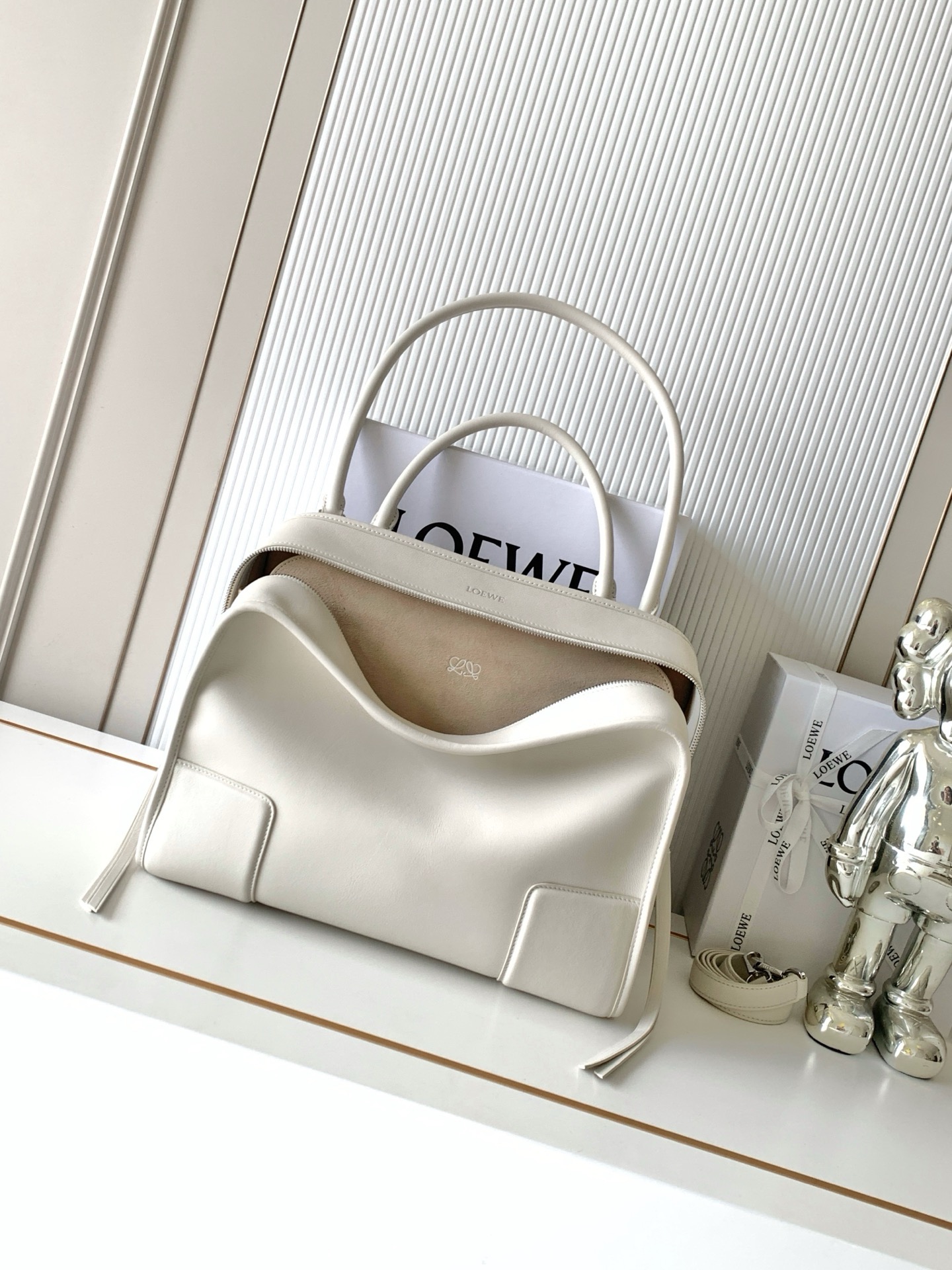 NO:854414,New large size soft cow leather Amazona 180 handbag, same style as Amazona stars  180 reinterprets the legendary handbag in a casual silhouette with a single top handle. The bag features an open design. The main compartment is secured with a hidden buckle and features a detachable shoulder and cross-body strap for a practical style. This large version is made from soft calfskin leather*3  Two ways to carry: Short handle, detachable shoulder and cross-body straps *Zipper with two leather zipper pulls*Two compartments, main compartment with magnetic closure  L embossed brand logo Size 34.5CM～27CM～14CM Style number 9173 Color white, Loewe, loewe, cowhide19860909新款大号柔软牛皮革 Amazona 180 手袋 明星同款Amazona 180重新诠释传奇手袋呈现休闲廓形,搭配单一顶部提手手袋采用开放式设计主隔层以隐藏扣固定搭配可拆卸肩背和斜挎背带打造实用风格.此大号版本采用柔软牛皮革制成*三种携带方式短提手、可拆卸肩背和斜挎背带*拉链配有两个皮革拉链头*两个隔层,主隔层以磁扣开合*内部扁平口袋*左侧D形环可定制*织物衬里*烫金或烫银,Double L 压纹品牌标志 尺寸34.5CM～27CM～14CM 款号9173 颜色白色,罗意威,loewe,cowhide,Bag