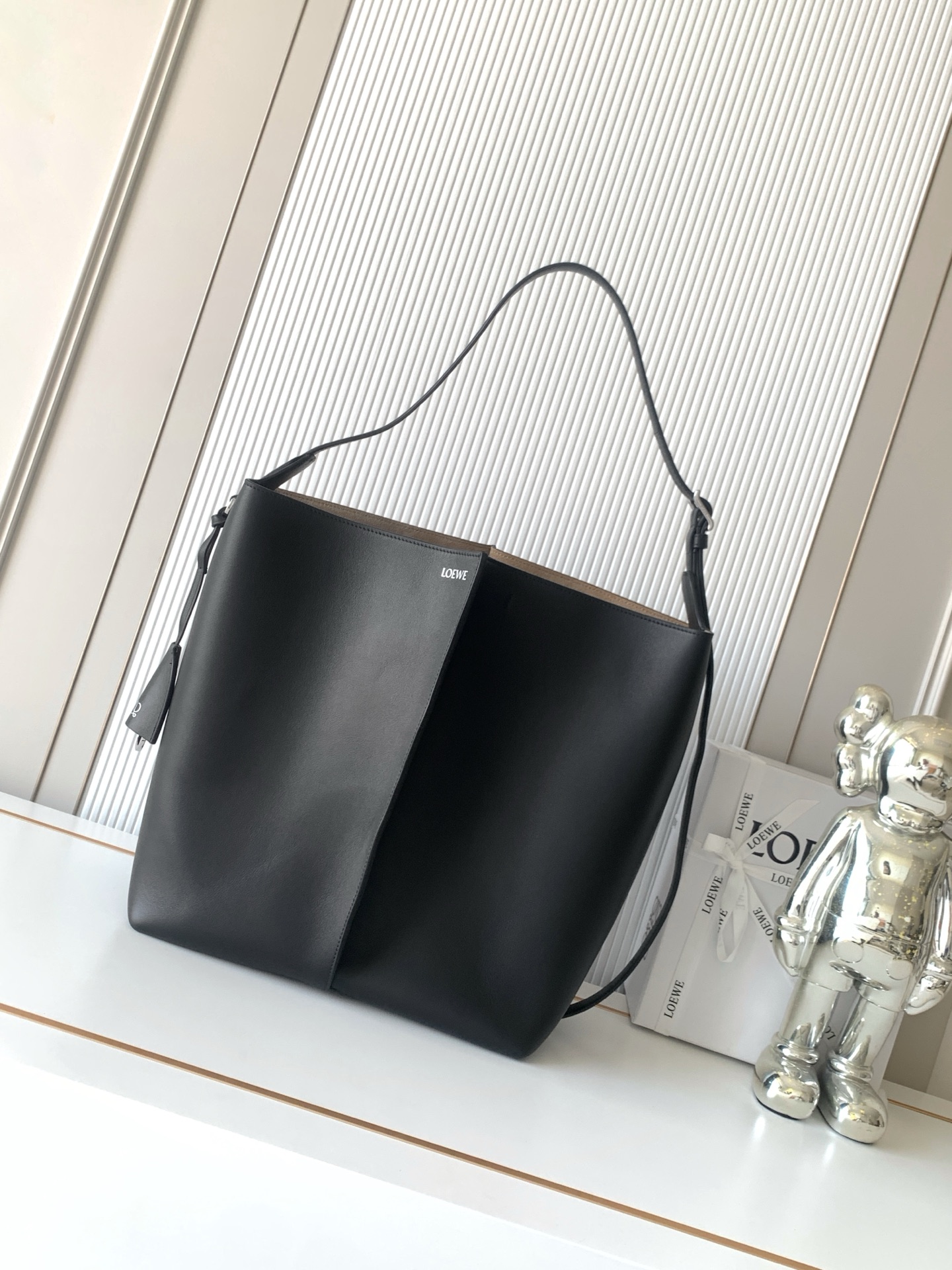 NO:854621,Large smooth cow leather Bilbao bucket bag Bilbao trapezoidal bucket bag, presenting a simple geometric design. Made of leather stitching with pleats in the middle. The shape is soft and close-fitting. Ideal for daily carry. This large version is made of smooth cow leather. * Can be worn on the shoulder or cross-body * Adjustable shoulder strap * Detachable Double L  Embossed leather bell-shaped pendant with built-in practical bottle opener. 'Extra external D-ring can be used to match personalized pendants. *Hook buckle to secure belongings.19860909大号光滑牛皮革 Bilbao 水桶手袋Bilbao 梯形水桶手袋,呈现简约几何设计采用皮革拼接打造,中间饰有褶裥,造型柔软贴身是日常随身携带的理想选择此大号版本采用光滑牛皮革制成*可肩背或斜挎*可调节肩带*可拆卸 Double L 压纹皮革钟形挂饰内藏实用开瓶器“额外的外部D形环可用于搭配个性化挂饰*钩扣可固定随身物品*绒面革衬里*烫银 款号9178 尺寸33CM～27.5CM～17CM 颜色黑色,罗意威,loewe,cowhide,Bag