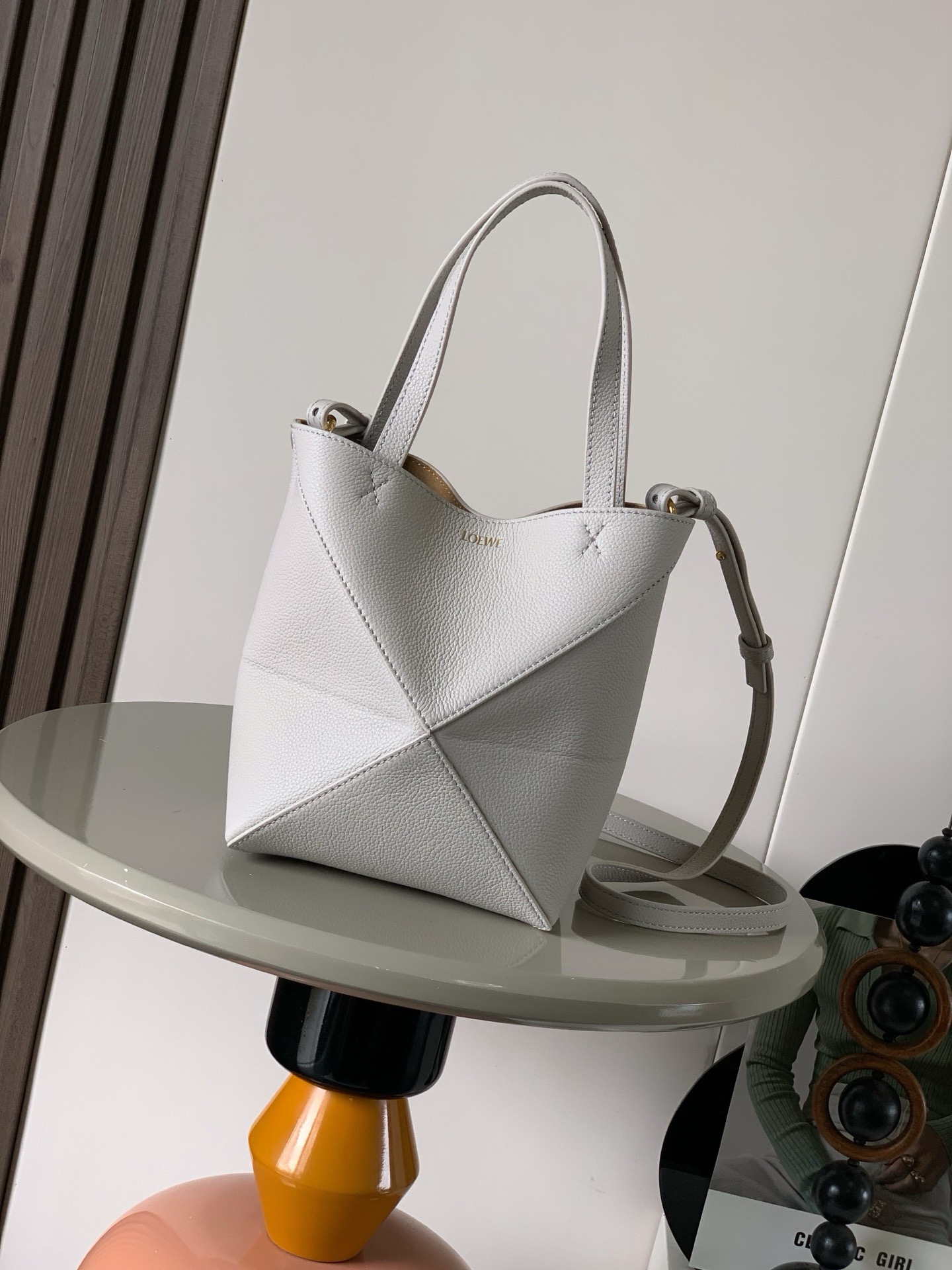 NO:919939,The new glossy cow leather mini puzzle Fold handbag plays with geometric patterns again. It has been a long time since I have seen such a practical and design tote bag. This one continues the geometric aesthetics of the Puzzle series. Inspired by the origami bag, this Puzzle Fold tote can switch between three-dimensional and flat surfaces at will. The leather is very delicate and shiny. It is ultra-light in weight, and the Puzzle can be folded.  The Fold handbag draws inspiration from the geometric lines of the brand's classic handbag series and uses creative ingenuity to reinterpret it into a fashionable tote bag that can be completely folded and is a good travel companion. This mini version is made of soft glossy cowhide, size 20CM ~ 16.5CM ~ 9CM, style number 9030, color light gray liche, Loewe, loewe, totes, cowhide19860909新款亮面牛皮革迷你号puzzle Fold手袋又把几何图形玩出花了很久没见过这么实用又设计感满满的托特包了这款延续了Puzzle系列的几何美学以折纸包为灵感,让这只 Puzzle Fold tote 在立体和平面随意切换皮质都很细腻光泽本身自重超轻,外加可以折叠Puzzle Fold手袋从品牌经典手袋系列的几何线条汲取灵感运用创意巧思将其重新诠释为一款时尚的托特袋,能完全折叠是旅行良伴.这个迷你号版本采用柔软的亮面牛皮革打造 尺寸20CM～16.5CM～9CM 款号9030 颜色浅轻灵灰荔,罗意威,loewe,totes,cowhide,Bag