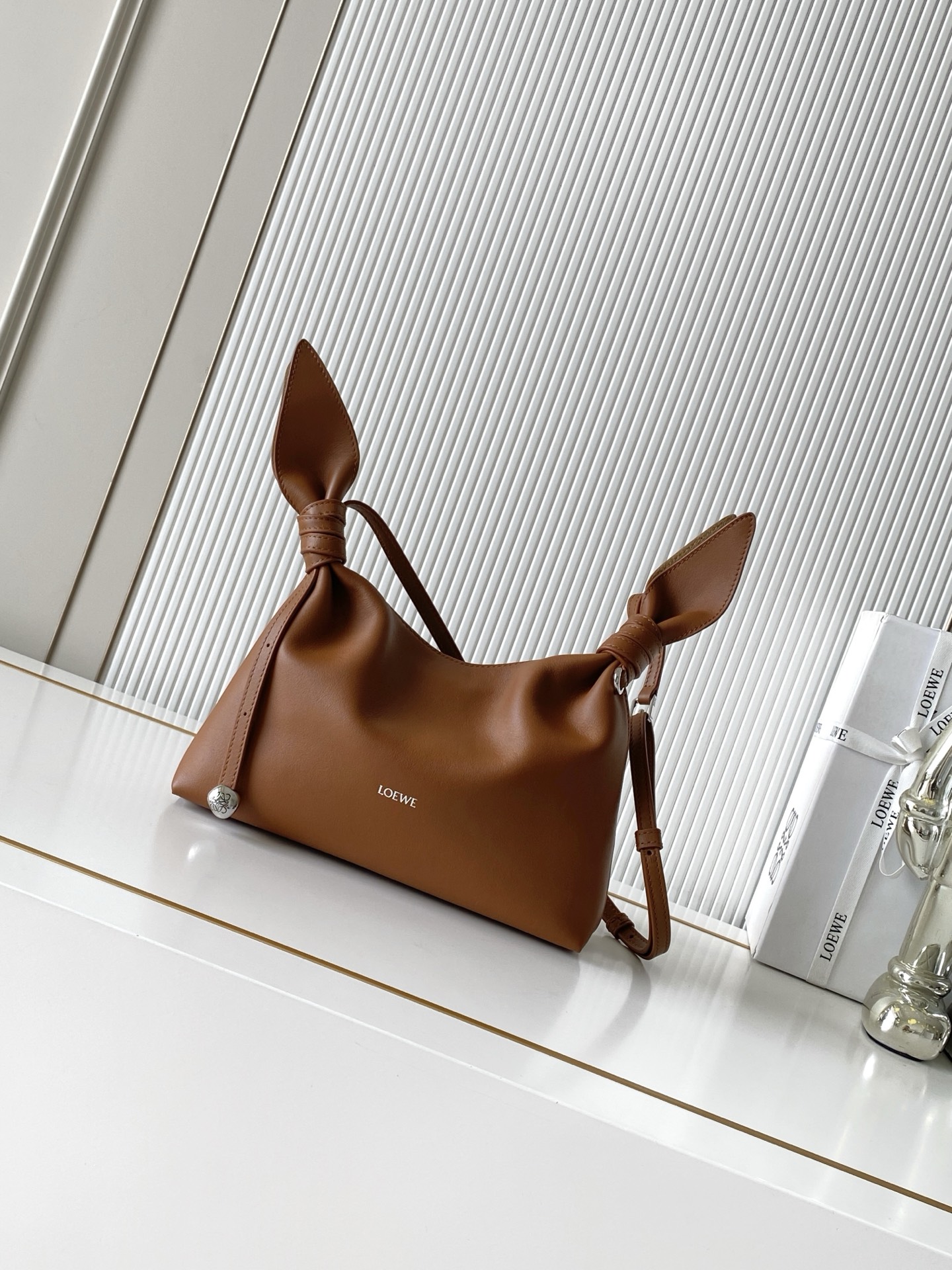 NO:941910,Mini Scarf bag in smooth calfskin The Scarf bag is made from two pieces of fabric, elegantly tied with leather knots and decorated with a new twist. The Pebble signature silhouette is clean, chic and feminine, reminiscent of a knotted scarf. This mini version is made of smooth calfskin *Adjustable leather strap*Can be worn by hand, shoulder or crossbody*Magnetic closure*Suede lining' Engraved Anagram Pebble *L0EWE Hot stamped or silvered  Size 24.5CM～14.5CM～6CM Style number 9187 Color squirrel brown, Loewe, loewe, cowhide19860909迷你号光滑牛皮革 Scarf 手袋Scarf手袋由两片布料构成透过皮革绳结优雅系合并饰有全新扭曲效果 Pebble 标志廓形简洁别致且充满柔美魅力让人不禁联想到系结围巾. 此迷你号版本采用光滑牛皮革制成*可调节皮革肩带*可手提、肩背或斜挎*磁扣开合*绒面革衬里“镌刻Anagram Pebble *L0EWE 烫金或烫银 尺寸24.5CM～14.5CM～6CM 款号9187 颜色松鼠棕,罗意威,loewe,cowhide,Bag