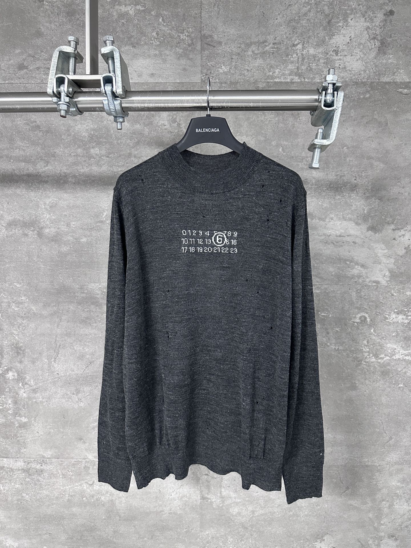 NO:538973,MM6: Magila 25FW Destruction Jacquard Wool Blend Sweater Detergent Spinning Special Gray Yarn, whose gray is by no means an ordinary color, is a special gray yarn specially designed for spinning. This gray is usually incorporated into the mixed-color spinning technology at the yarn spinning stage to create a rich, deep and subtle layered 'dirty gray'. It avoids the blandness of a single gray, gives the fabric a natural antique texture like an old object, and provides a perfect color base for subsequent destruction treatments. The wool blend formula is carefully calculated. High proportions of merino wool provide a delicate and soft touch and warmth, while a small amount of other fibers mixed in are designed to enhance the strength, support, or bring a unique fluffy luster to ensure that subsequent hole treatments can be precisely controlled rather than overall collapse.  The chest pattern adopts a precision jacquard process, which is woven at one time, rather than post-dyeing. This means that the pattern is formed directly by the weaving process by the complex warp and weft interlacing during the knitting process. The needle method is extremely precise, integrating inlay technology to achieve a smooth transition of large color blocks, and combining the hanging needle three-dimensional needle method to create subtle texture changes in the planar pattern. The jacquard pattern itself often continues Margiela's abstract and symbolic style, which may be a fuzzy number, a deformed symbol or a seemingly disordered code. The design is cleverly that it is both a visual focus and provides a 'target' for subsequent destruction. The overlap between the hole and the pattern produces a new and unpredictable visual effect. Post-destruction  This is the most complex and unconventional step in the whole work. All damage treatments are done by craftsmen after the sweater is completely woven into shape. This is essentially different from the simple method of 'breaking first and then knitting', which requires craftsmen to have an extreme understanding of the tension, elasticity and dispersion of the knitted structure. Craftsmen will use special tools (such as grinding needles, grinding wheels, tweezers, etc.) to accurately grind the surface yarn in a specific area, and try to retain the base layer inside. This process requires extremely high skills to control the size, shape and wear of the hole, and simulate the wear effect formed during natural wear, but it is more artistic and visual impact.  The final product presents a decadent aesthetic after careful calculation. Every hole and every burr is not accidental, but the final result of being carefully designed and executed. It tells a story about time, wear and eternity, a collection-level fashion work that combines top textile technology, advanced handicrafts and profound conceptual thinking. Size S M L,,masion margiela,masion margiela,sweaters,alexander wang19860909MM6:马吉拉 25FW 破坏提花羊毛混纺毛衣 定纺特殊灰色纱线,其灰色绝非普通色号,而是专门定纺的特殊灰度纱线.这种灰色通常是在纱线纺纱阶段就融入混色纺纱技术,营造出一种丰富、深沉且具有微妙层次感的“脏感灰”.它避免了单一灰色的平淡,赋予面料一种天生的、如同旧物般的古董质感,为后续的破坏处理提供了完美的色彩基底. 羊毛混纺的配方经过精心计算.高比例的美利奴羊毛提供细腻柔软的触感和保暖性,而混入的少量其他纤维则旨在增强纱线的强韧性、支撑力或带来独特的绒毛光泽,确保后续的破洞处理能够精准可控,而非整体崩塌. 胸前图案采用精密提花工艺,一次性织就,而非后期印染.这意味着图案是由不同颜色的纱线在编织过程中通过复杂的经纬交错直接形成.针法极其精密,融合了嵌花技术来实现大色块的平滑过渡,并结合挂针立体针法在平面图案中创造微妙的肌理变化. 提花图案本身往往延续Margiela的抽象、符号化风格,可能是一个模糊的数字、一个变形的符号或一段看似无序的代码.其设计巧妙在于,它既是视觉焦点,也为后续的破坏提供了“目标”,破洞与图案的交叠产生了全新的、不可预知的视觉效果. 后置式解构 这是整件作品最复杂且反常规的一步.所有破坏处理都是在毛衣完全织造成型后,由工匠手工完成的.这与“先破再织”的简单方式有本质区别,要求工匠对针织结构的张力、弹性和脱散性有极致理解. 工匠会使用特制的工具（如磨针、砂轮、镊子等）在特定区域精准地磨断表面的纱线,而尽量保留内部的基底层.这个过程需要极高的技巧,以控制破洞的大小、形状和磨损程度,模拟出自然穿着中形成的磨损效果,但更具艺术性和视觉冲击力. 最终成品呈现出的是一种精心计算后的颓废美学.每一处破洞、每一缕毛边都并非偶然,而是被精心设计和执行的最终结果.它讲述了一个关于时间、磨损和永恒的故事,是一件融合了顶尖纺织技术、高级手工技艺和深刻概念思考的收藏级时装作品. 尺码S M L,,masion margiela,masion margiela,sweaters,alexander wang,Men's clothing