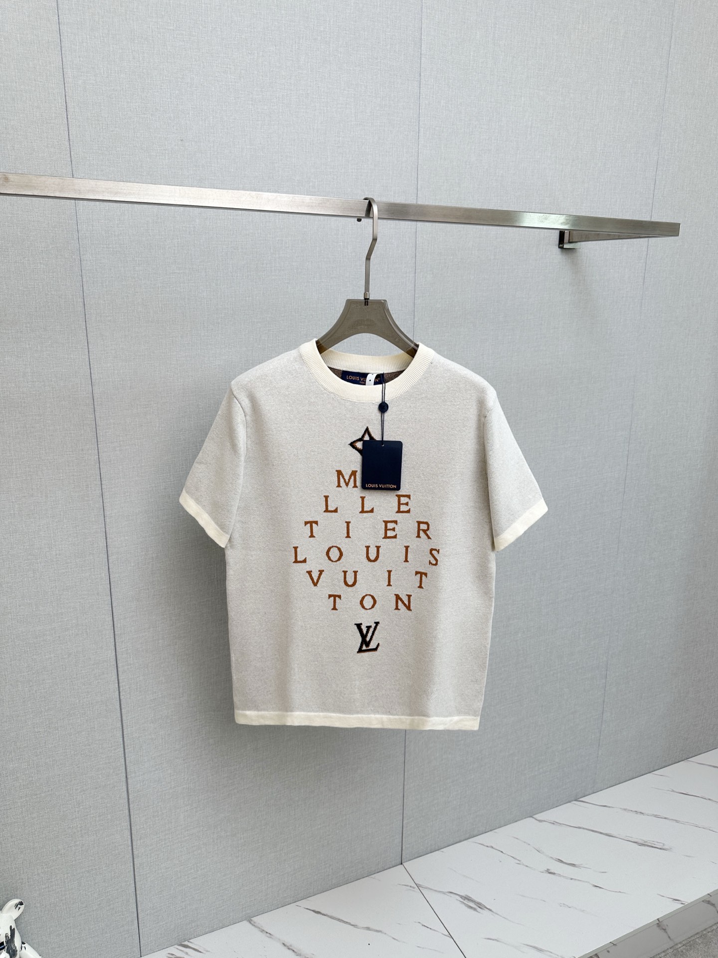 NO:957088,LV Atelier series letter jacquard knitted short sleeves restore the design language of the LV Atelier workshop series. The front adopts 'MALLETIER LOUIS VUITTON' staggered letter jacquard, with the four-leaf flower at the top and the LV logo at the bottom, restoring the retro aesthetics of the brand's workshop culture. The high-density jacquard process restores the details, and the knitting lines are smooth and clear without jumper misalignment; the loose straight version modifies the body shape, whether it is daily casual or street wear, you can easily wear LV's retro high-end feel. Size  Xs-L,,louis vuitton,louis vuitton,T-shirt,19860909LV Atelier系列字母提花针织短袖 还原LV Atelier工坊系列设计语言,正面采用“MALLETIER LOUIS VUITTON”错落字母提花,搭配顶部四叶花与底部LV标识,还原品牌工坊文化的复古美学.高密度提花工艺还原级细节,织线平整清晰无跳线错位；宽松直筒版型修饰身形,无论是日常休闲还是街头穿搭,都能轻松穿出LV的复古高级感. 尺寸 Xs-L,,louis vuitton,louis vuitton,T-shirt,,Men's clothing