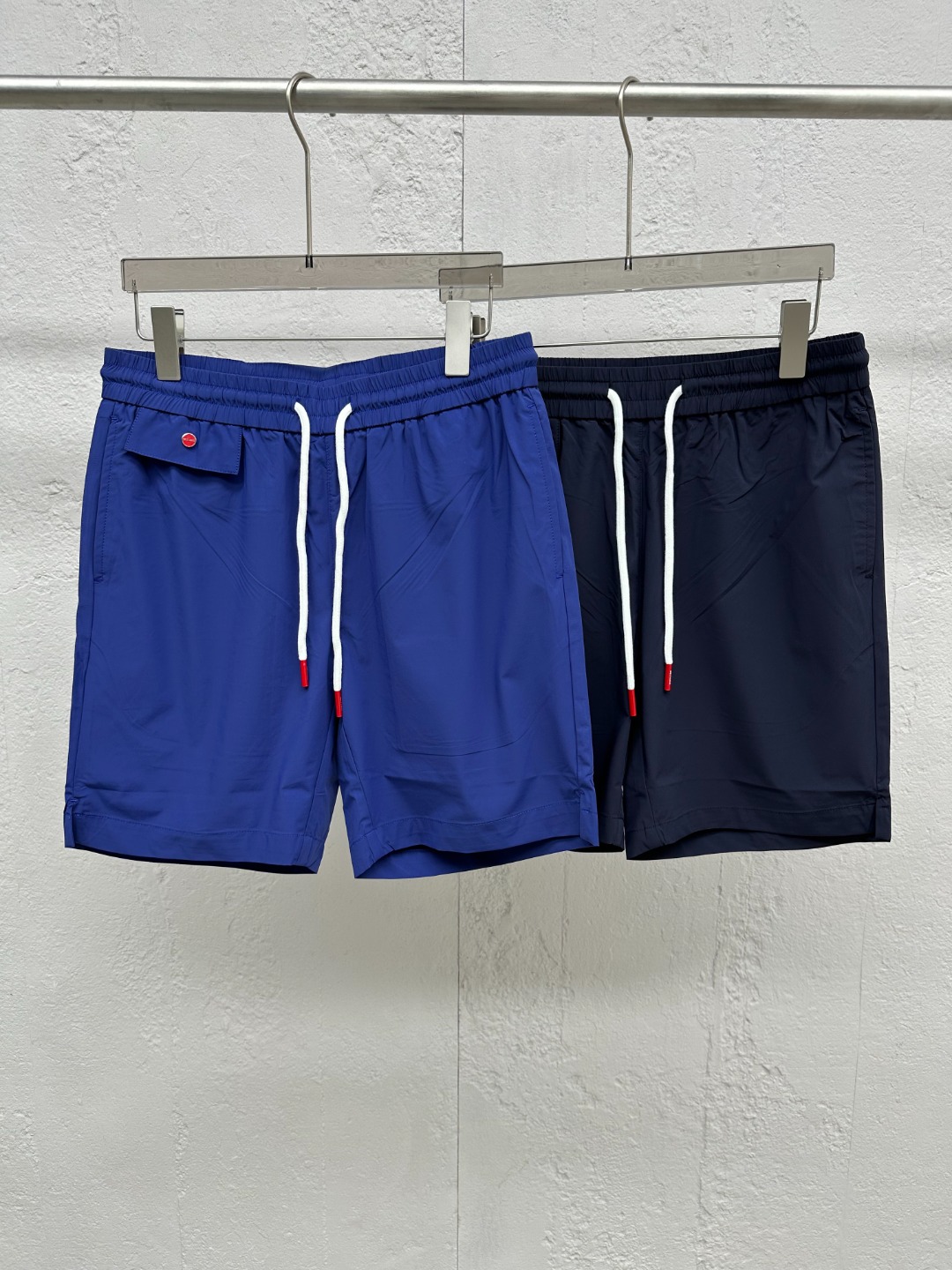 NO:830489,[New Product] Goods from trading company channels, originally produced in Italy, 2026 spring and summer new KITON men's classic red button decoration, thin technical woven fabric drawstring shorts, three-quarter pants!  These shorts are made of custom-made technical woven fabric, which is not only light and delicate in texture, fits like a second layer of skin, but also has excellent comfort and breathability!  Even in the hot summer, it can ensure that the wearer enjoys a refreshing feeling like the breeze blowing on the face!  Red buttons adorn the front, which are not only bright in color, but also complement the enthusiasm of summer. The details highlight your distinguished status!  Even more unique is the design of the rope-head hanging clock, which cleverly incorporates brand elements. It is small and exquisite. It sways gently with the steps, as if whispering the brand's story. It is both fashionable and eye-catching!  It perfectly echoes the embroidered letter logo on the back pocket. The embroidery craftsmanship is exquisite and the letter lines are smooth. It not only adds to the artistic sense of the shorts, but also deeply demonstrates the brand tone and cultural heritage of KITON!  The pattern adopts a drawstring elastic waistband design. This design not only gives the wearer greater freedom, and can easily adjust to the most comfortable tightness whether it is daily leisure or outdoor activities, but also adds a bit of casualness and uninhibitedness to the overall look!  The straight version design cleverly modifies the leg lines. Whether you are tall or medium-sized, you can easily control it, showing a simple yet stylish fashion attitude!  Color dark blue light blue Size M L  XL waist 82/88cm - hip 106cm - front 28cm - thigh 62cm - trouser length 45cm XXL waist 85/91cm - hip 110cm - front 29cm - thigh 64cm - trouser length 46cm 3XL waist 88/94cm - hip 114cm - front 29cm - thigh 66cm - trouser length 47cm,,shorts,19860909【新品】贸易公司渠道货,意大利原厂出品,2026春夏新款KITON奇顿男士经典红色纽扣装饰轻薄科技梭织面料抽绳短裤,五分裤！这款短裤采用的是客供定制的科技梭织面料,不仅质地轻薄细腻,如同第二层肌肤般贴合,还拥有着卓越的舒爽透气性！即便是炎炎夏日,也能确保穿着者享受如微风拂面般的清爽感受！红色纽扣点缀前幅,不仅色彩鲜明,与夏日的热情相得益彰,细节之处彰显尊贵身份！更为独特的是绳头吊钟的设计,它巧妙地融入了品牌元素,小巧而精致,随着步伐轻轻摇曳,仿佛在低语品牌的故事,既时髦又抢眼！与后兜上的刺绣字母标识形成了完美的呼应,刺绣工艺精湛,字母线条流畅,不仅增添了短裤的艺术感,更深刻地展现了KITON的品牌调性与文化底蕴！在版型上采用了抽绳松紧裤腰设计,这一设计不仅赋予了穿着者更大的自由度,无论是日常休闲还是户外活动,都能轻松调节至最舒适的松紧度,同时也为整体造型增添了几分随性与不羁！直筒的版型设计,则巧妙地修饰了腿部线条,无论是高挑身材还是中等体型,都能轻松驾驭,展现出简约而不失格调的时尚态度！ 颜色深蓝色 浅蓝色 尺码M L XL XXL XXXL 尺码数据 M码腰围76/82cm-臀围98cm-前档27cm-大腿围60cm-裤长43cm  L码腰围79/85cm-臀围102cm-前档28cm-大腿围61cm-裤长44cm  XL码腰围82/88cm-臀围106cm-前档28cm-大腿围62cm-裤长45cm  XXL码腰围85/91cm-臀围110cm-前档29cm-大腿围64cm-裤长46cm  3XL码腰围88/94cm-臀围114cm-前档29cm-大腿围66cm-裤长47cm,,shorts,,Men's clothing
