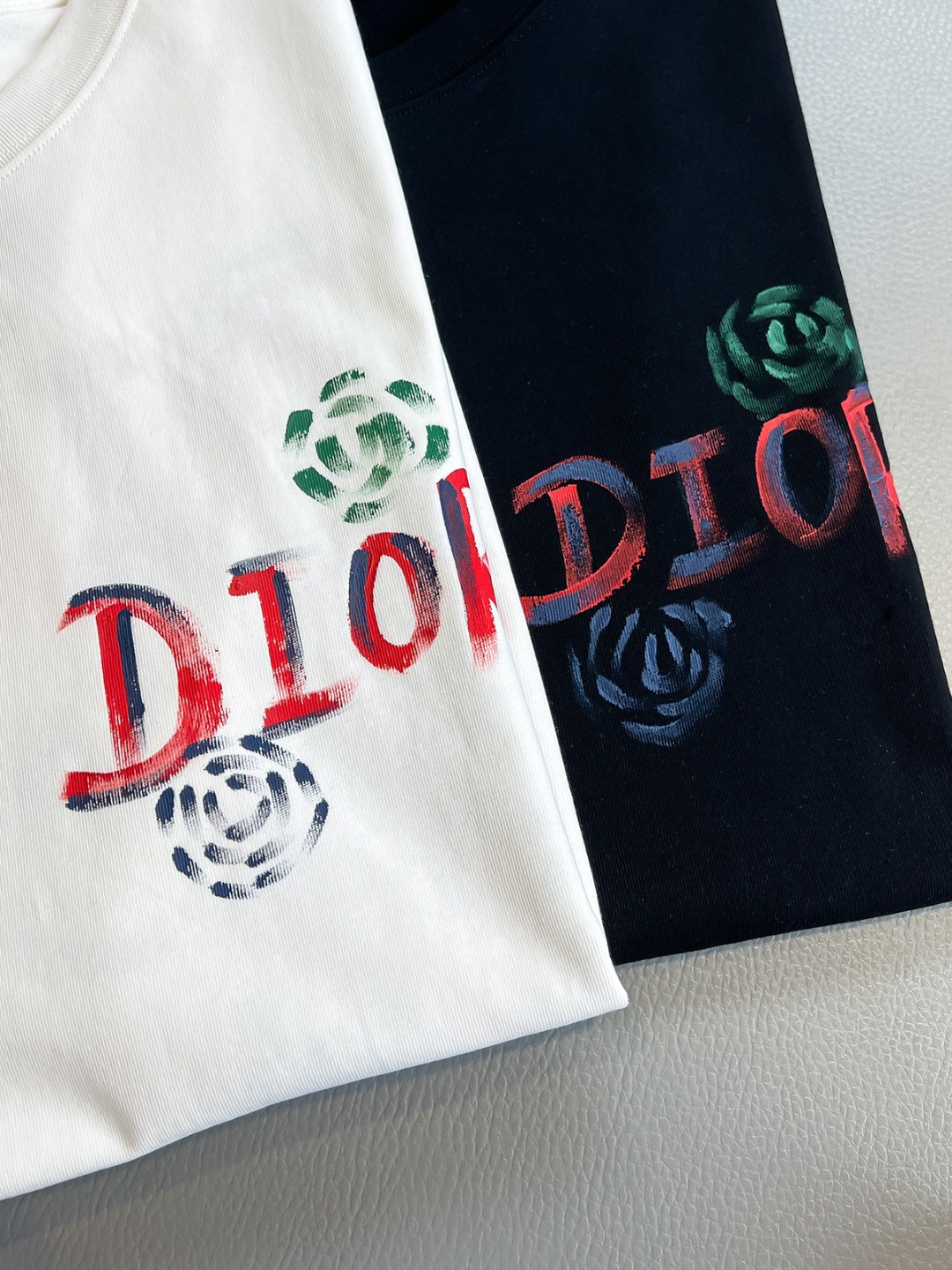 P120🍀【新品】贸易公司洋行货，重磅高级心水之物，2025春夏新款Di*r 手绘彩色标识印花男士短袖T恤。CD经典时髦字母风潮,凝聚独特技艺与灵巧的创意.简约而不失精炼风范…胸前Di*r 数码印花立体美观,后背Di*r 花卉印花,视觉效果彰显百态的奢华体验.平纹针织棉面料,细致工艺技术最高的面料标准.完美细腻的质感让着身更为舒适透气.现代休闲化裁剪工整细致,铸就独特造型魅力.
颜色：黑色 白色 
尺码：S M L XL XXL
尺码数据：
S码:胸围102cm-肩宽45cm-衣长69cm-袖长22cm
M码:胸围106cm-肩宽46cm-衣长70cm-袖长23cm
L码:胸围110cm-肩宽47cm-衣长71cm-袖长24cm
XL码:胸围114cm-肩宽48cm-衣长72cm-袖长25cm
XXL码:胸围118cm-肩宽49cm-衣长73cm-袖长26cm