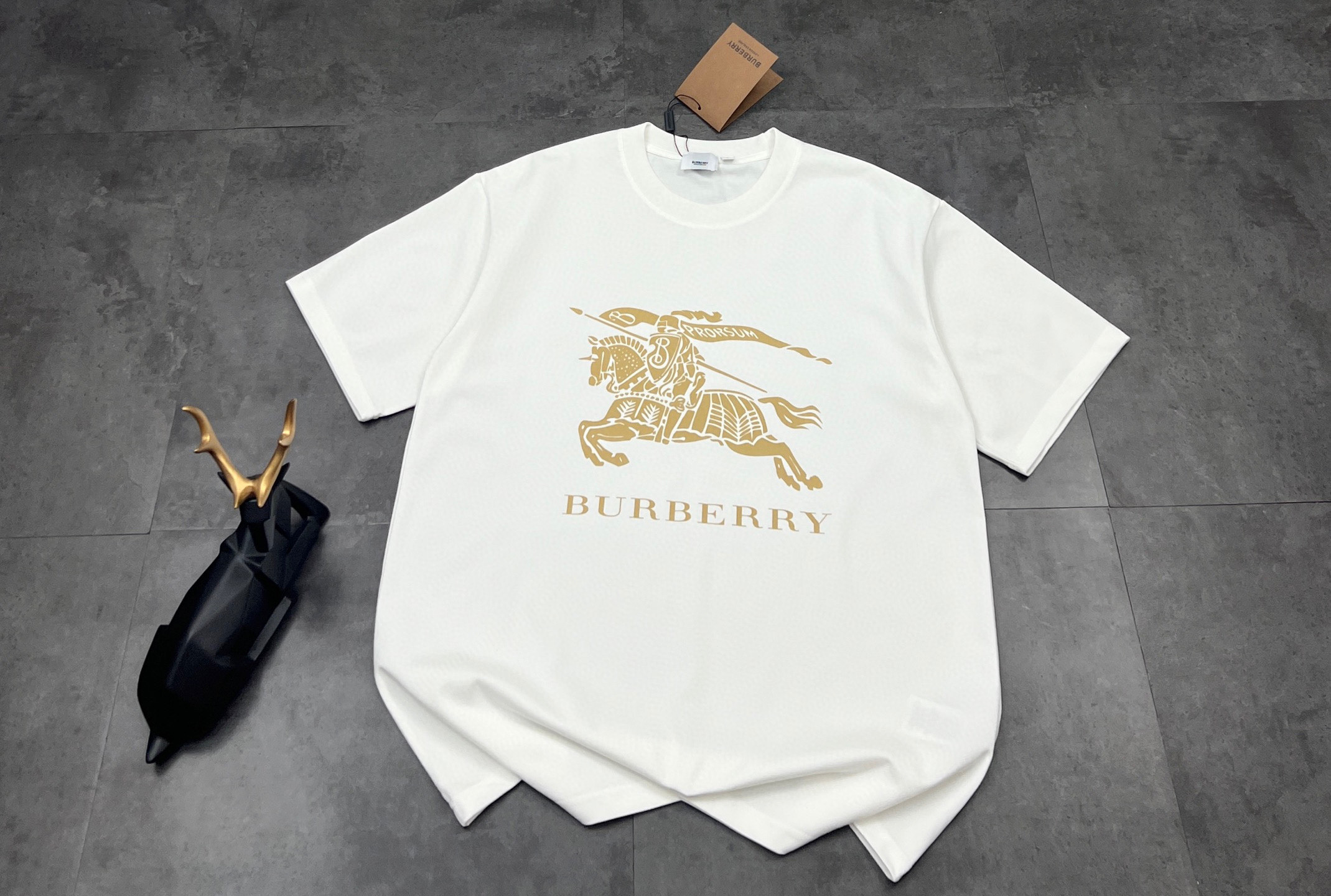💰85
👑新款短袖上新🆕25ss夏季新品BURBERRY 🐎巴宝莉骑士tee，经典永流传，简直是时尚圈的“常青树”🌲

260g双纱面料，质感直接拉满💯  软糯又挺括，贴身穿像被云朵轻轻包裹☁️  厚度刚好，四季穿都很奈斯，不会软塌塌没型，高级感拿捏～

经典骑士图案🏇  金色印花超精致，战马奔腾的设计，自带英伦贵族气场，走在街上，回头率爆棚📸  不管是搭牛仔裤走休闲风，还是配西装裤凹轻商务造型，都能稳稳hold住，轻松拿捏各种风格切换✨

印花工艺也很绝，久洗不易脱落、开裂，经得住时间考验⌛️  就像巴宝莉的品牌魅力，历久弥新，穿个几年依旧是衣柜里的“宝藏单品”💎

喜欢经典款、追求品质的宝子，别错过！穿上它，你就是行走的时尚教科书，把高级感焊在身上～

颜色：黑色/白色
尺码：M  L  XL  2XL

M：胸围54  肩宽52   衣长70   袖长22.5
（建议身高170-173厘米）
（建议体重110-135斤）
L：胸围 56  肩宽54   衣长72  袖长23
（建议身高173-175厘米）
（建议体重135-160斤）
XL：胸围58  肩宽56  衣长74  袖长23.5
（建议身高175-180厘米）
（建议体重160-185斤）
2XL：胸围60  肩宽58  衣长76   袖长24 
（建议身高180-185厘米）
（建议体重185-210斤）
👑温馨提示:手工平铺测量，误差在1-2cm内属于正常范围
