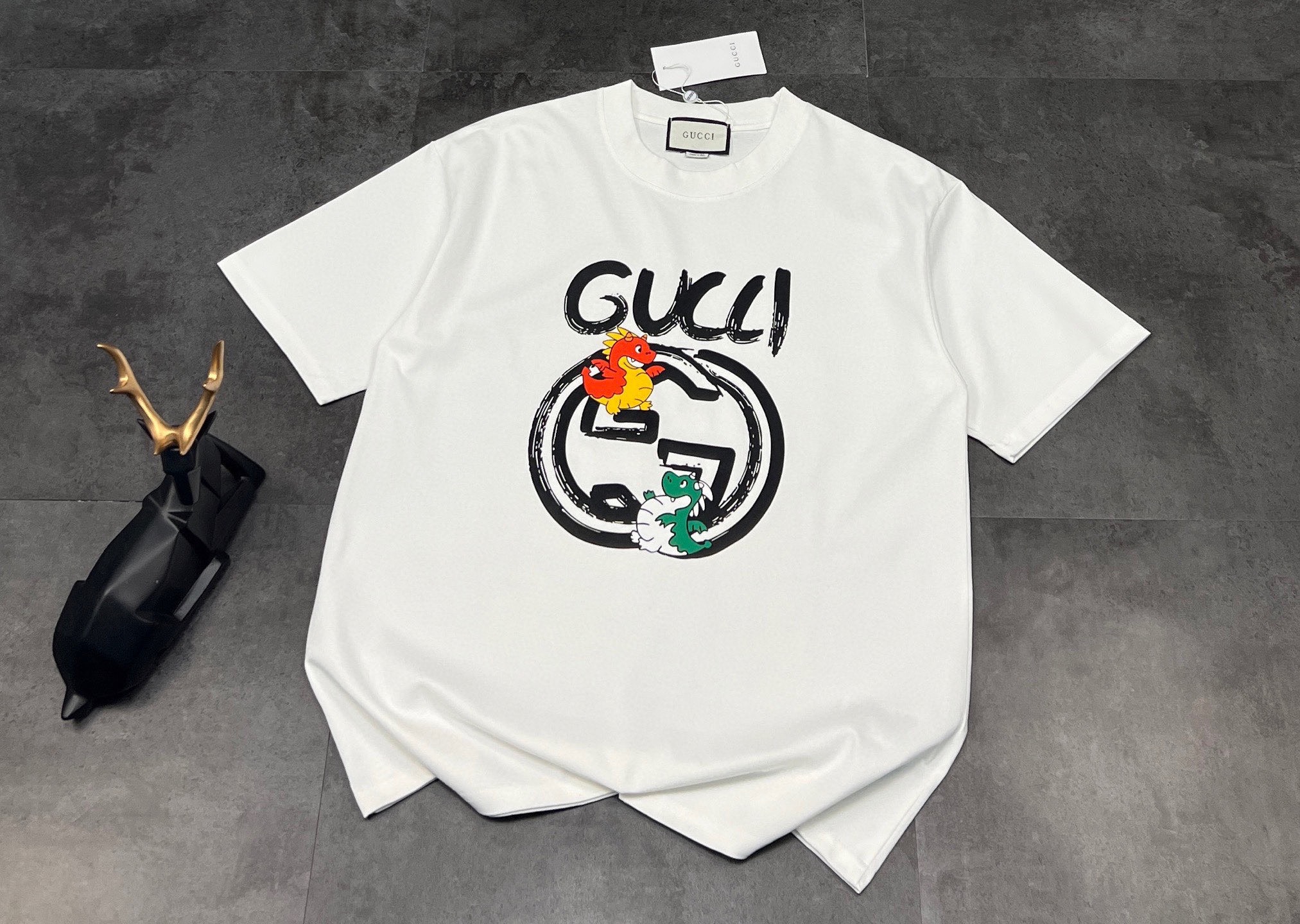 包邮 👑新款短袖上新🆕🆕 2026SS古驰GUCCI 新品!家人们,我不允许还有人没get到这件古驰T恤👕 最近的心头好,走到哪被夸到哪~ 👚款式:经典的圆领短袖设计,简约又百搭,不挑人穿,无论是日常出街还是度假旅行,都能轻松适配各种场合.宽松的版型上身超舒服,自带慵懒感,藏肉又显瘦. 🧵面料:采用双纱面料,质感超绝👍 摸起来柔软又厚实,垂坠感十足,而且透气性也很棒,夏天穿一点都不会闷热,久穿也不容易变形. 胸前独特的涂鸦风“GUCCI”字母搭配可爱的卡通小恐龙和经典双G标志,童趣中又不失时尚感,把潮流和复古完美融合,谁穿谁好看~ 定制260g同缸染面料,手感非常舒服,最新砖柜同步,OS落肩版型 时尚又个性,超级百搭好看的一款!男女都非常合适 人手必备款 吊牌 领标 水洗麦 三标齐全 颜色:黑色/白色 :胸围54 肩宽52 衣长70 袖长22.5 (建议身高170-173厘米) (建议体重110-135斤) L:胸围 56 肩宽54 衣长72 袖长23 (建议身高173-175厘米) (建议体重135-160斤) XL:胸围58 肩宽56 衣长74 袖长23.5 (建议身高175-180厘米) (建议体重160-185斤) 2XL:胸围60 肩宽58 衣长76 袖长24 (建议身高180-185厘米) (建议体重185-210斤) 👑温馨提示:手工平铺测量,误差在1-2cm内属于正常范围
