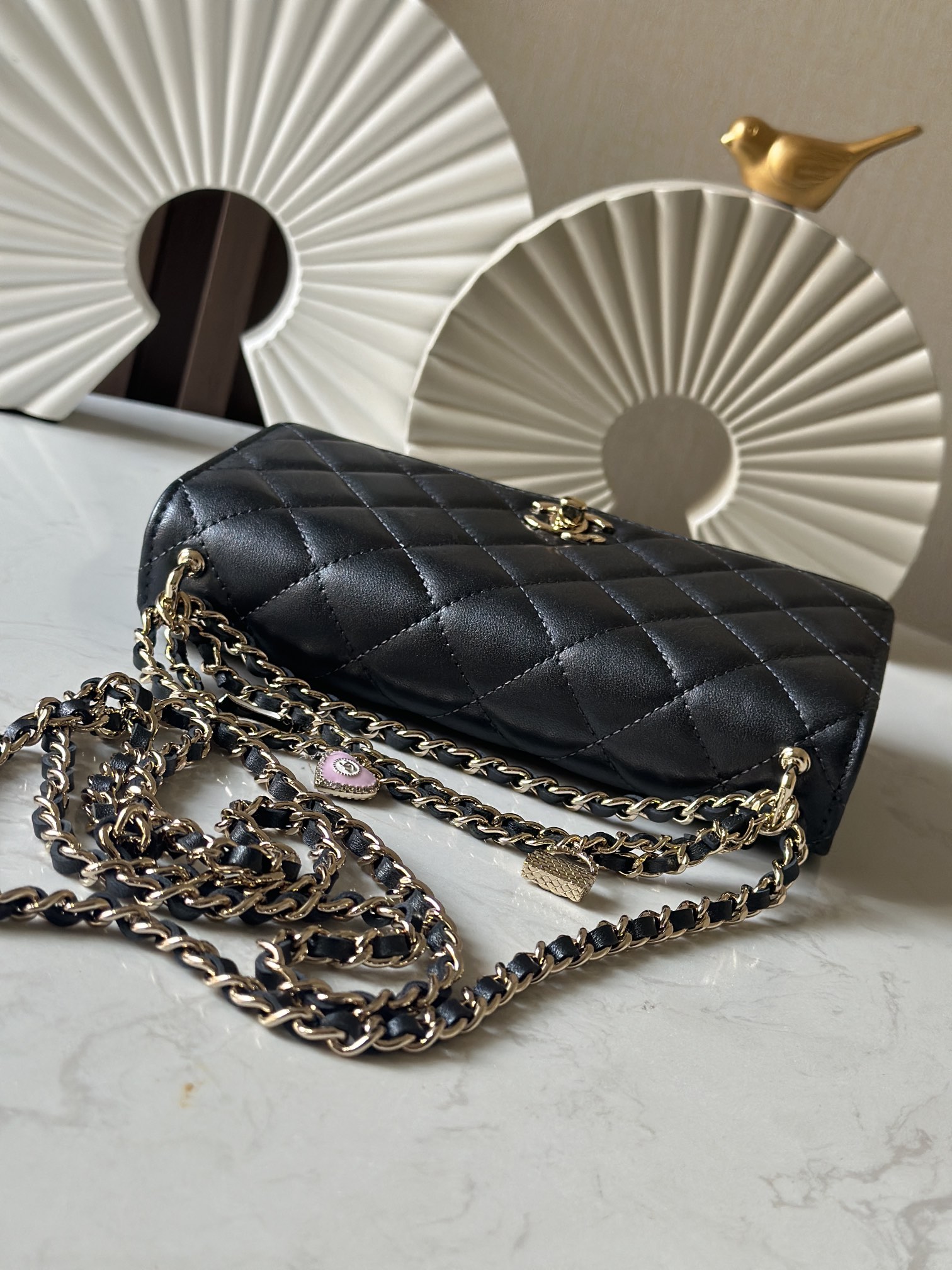 p670。chane12025春夏
chanel 太懂少女心!2025年春夏的轻巧俏
皮又精致，采用珠面小羊皮，搭配经典的菱格纹和金色 clogo。手袋上还有一个粉色心形，搭配金色链条，让人一见倾心，入坑!还可
以侧背或肩背，容量也不错，纸巾都可以放进去，通勤日常都ok
款号：66051 黑色
尺寸:19.5*13*3.5
