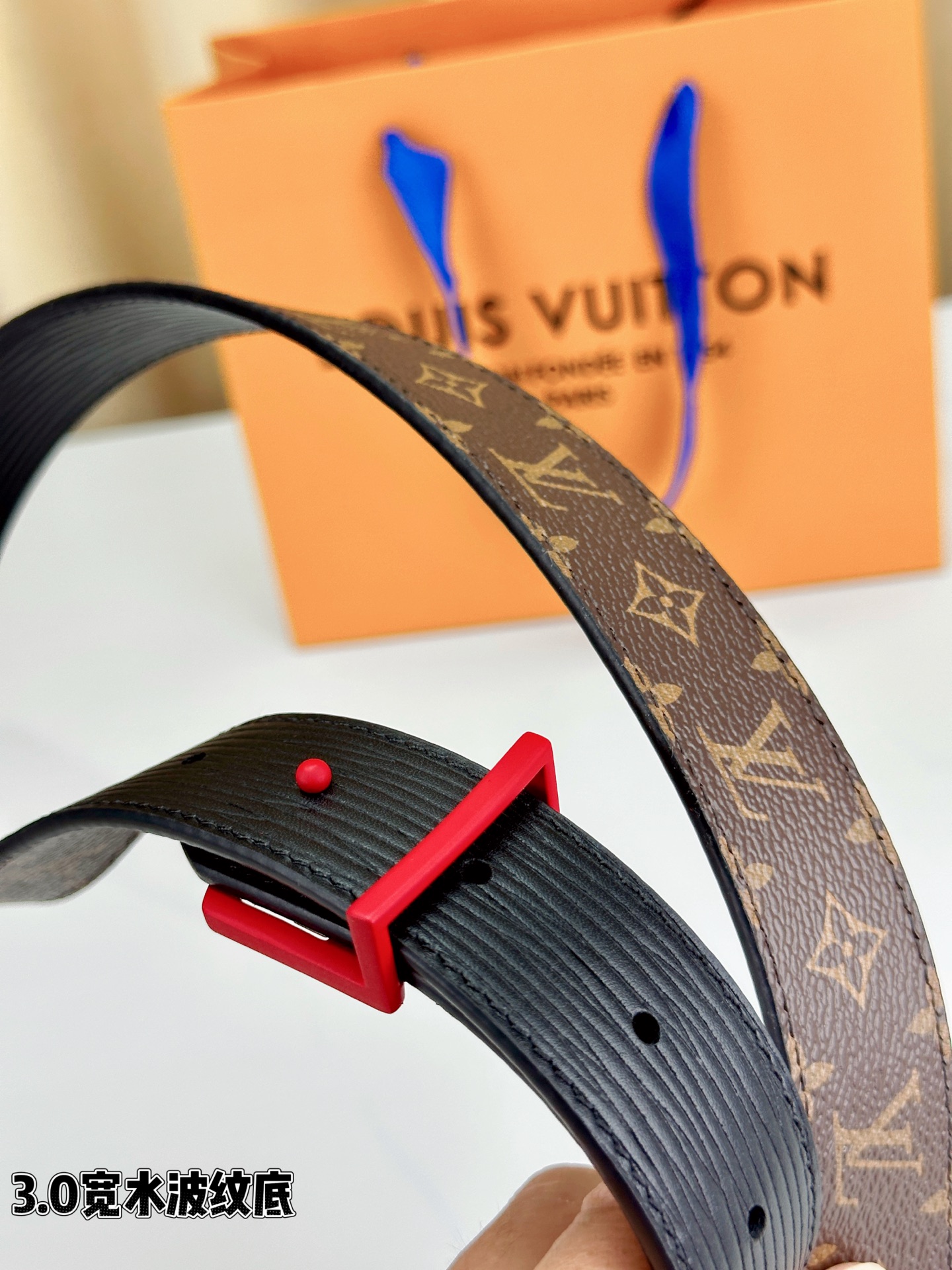经典棕底水波纹压花邂逅亮眼红扣，3.0cm宽幅设计勾勒腰线。LV标志性字母扣点缀，皮革触感细腻。1854