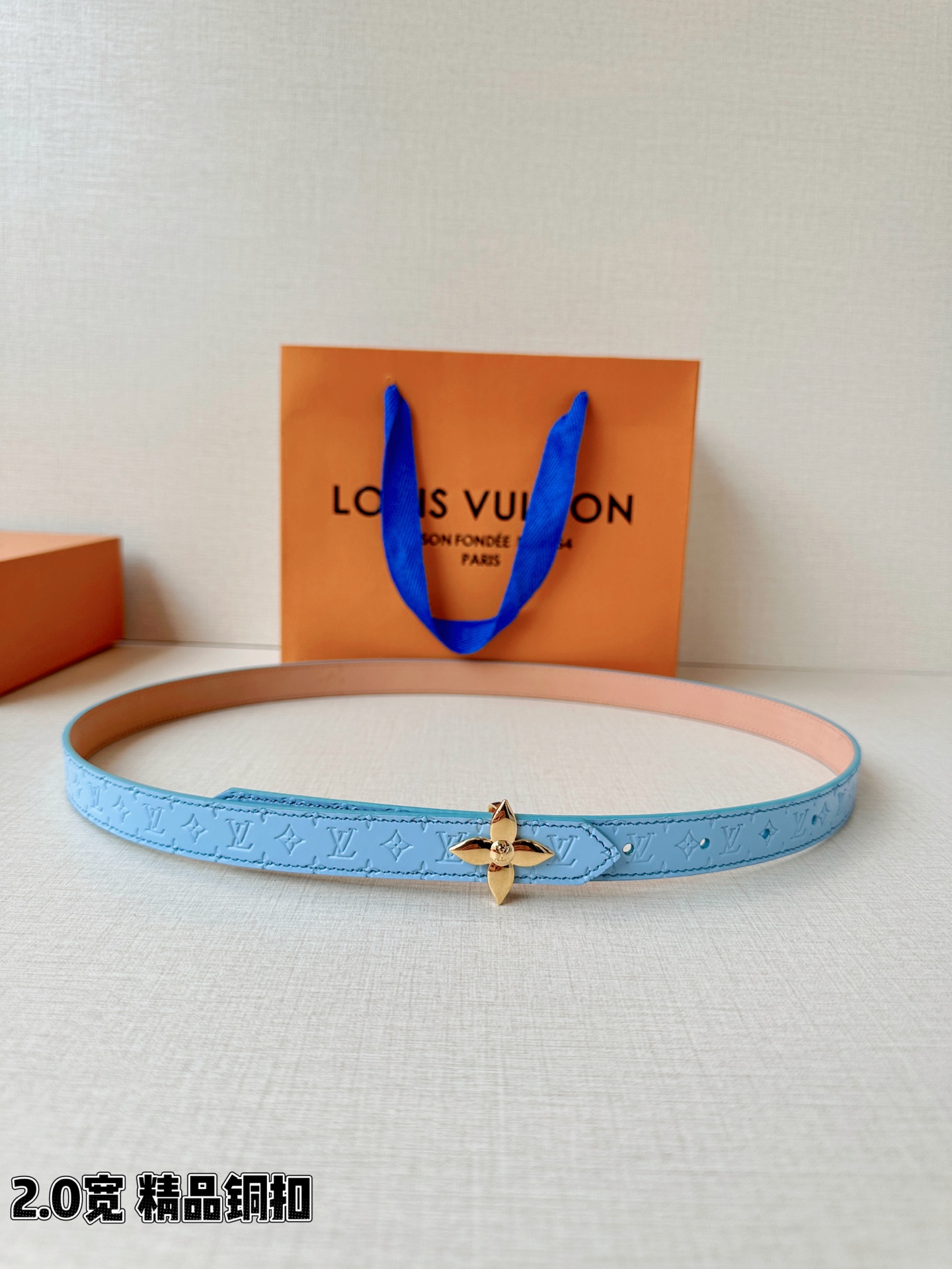 浅蓝色与米白色压纹皮革交织，2.0厘米纤细宽度勾勒腰线。金色铜质四叶花扣头，镌刻经典LV字母与菱形暗纹，