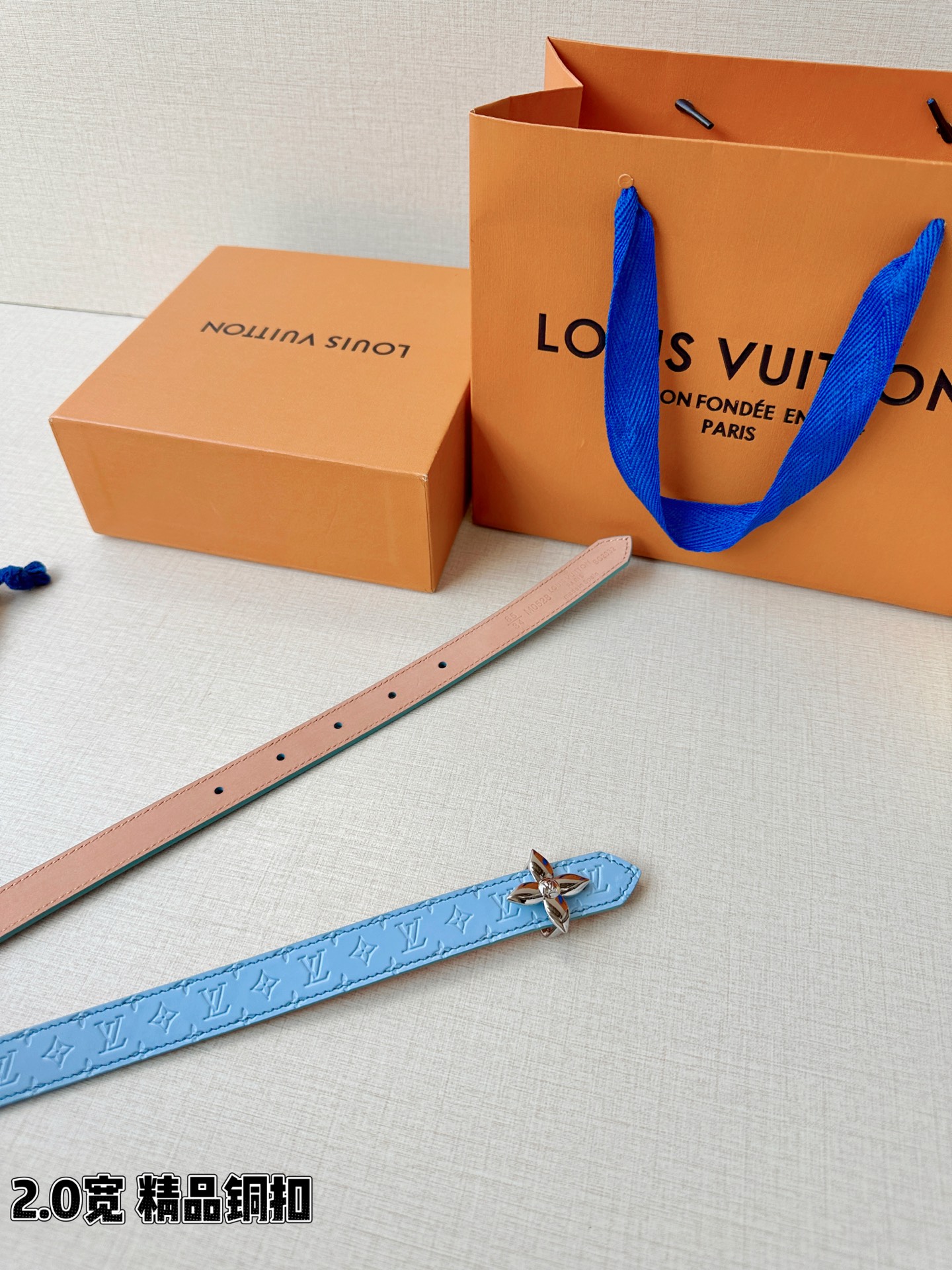 浅蓝色与米白色压纹皮革交织，2.0厘米纤细宽度勾勒腰线。金色铜质四叶花扣头，镌刻经典LV字母与菱形暗纹，