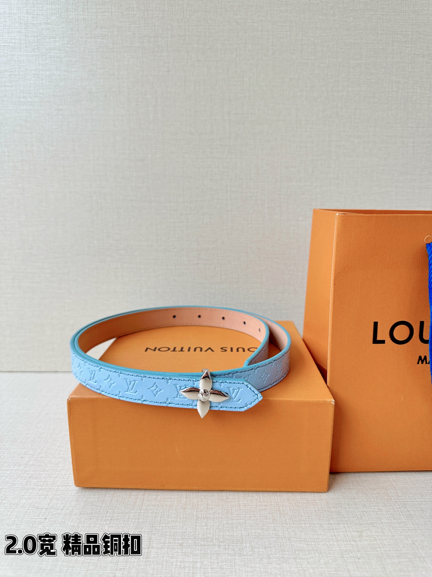 浅蓝色与米白色压纹皮革交织，2.0厘米纤细宽度勾勒腰线。金色铜质四叶花扣头，镌刻经典LV字母与菱形暗纹，