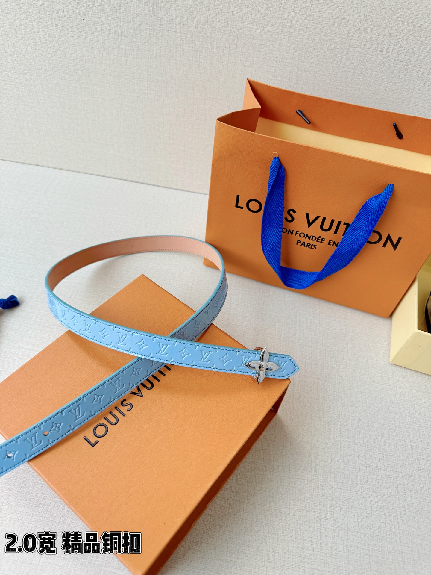 浅蓝色与米白色压纹皮革交织，2.0厘米纤细宽度勾勒腰线。金色铜质四叶花扣头，镌刻经典LV字母与菱形暗纹，